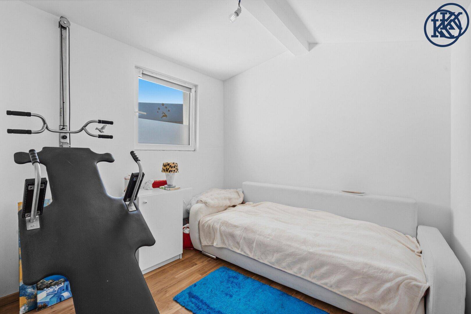 Schlafzimmer mit Einzelbett, Holzboden und einem Fenster, das Tageslicht hereinlässt.