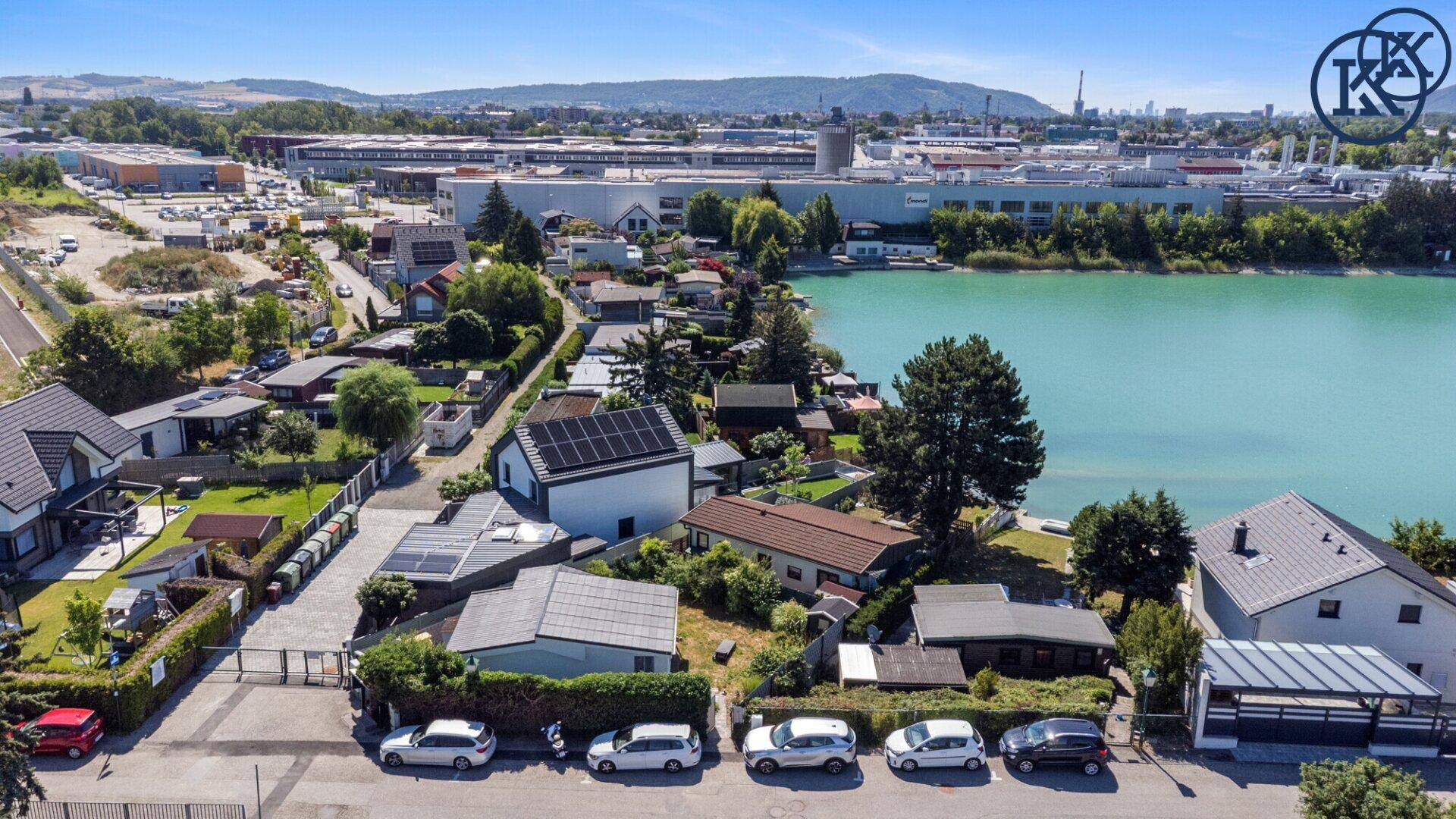 Luftaufnahme einer Wohnsiedlung am Seeufer mit angrenzendem Industriegebiet und Parkplätzen.