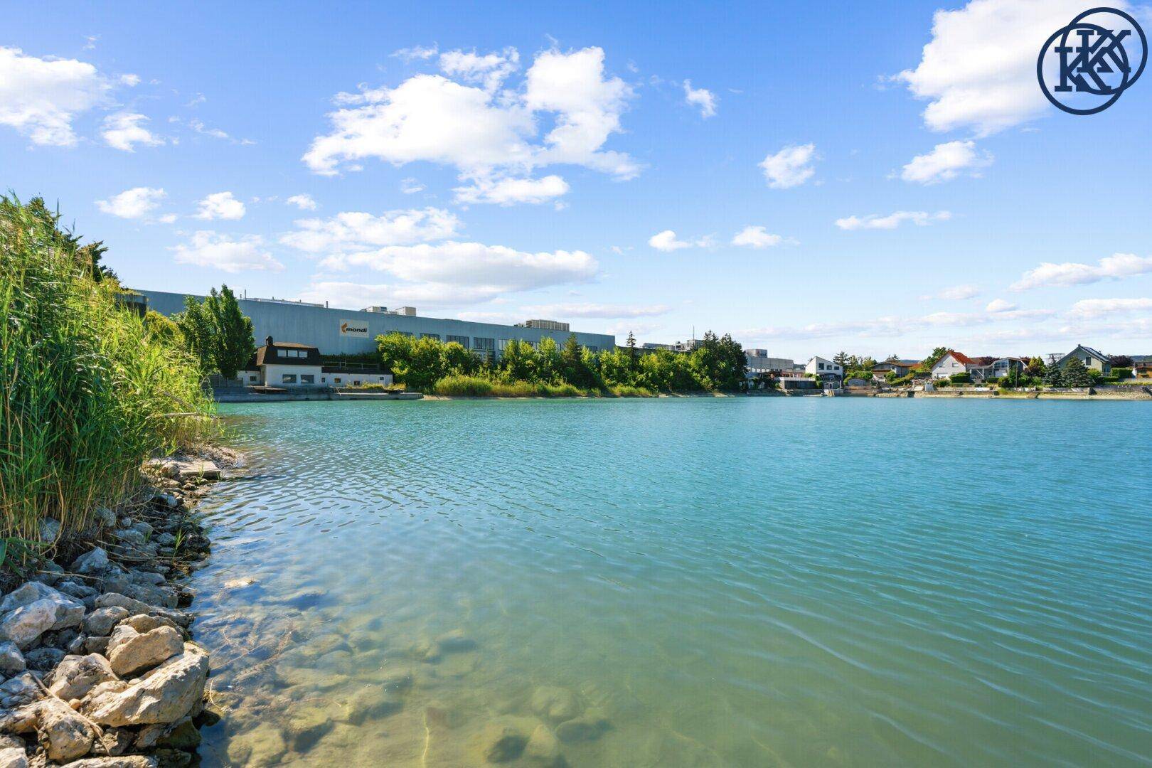 Weitläufiger Seeblick mit Industriegebäuden im Hintergrund und Wohnbebauung am rechten Ufer.