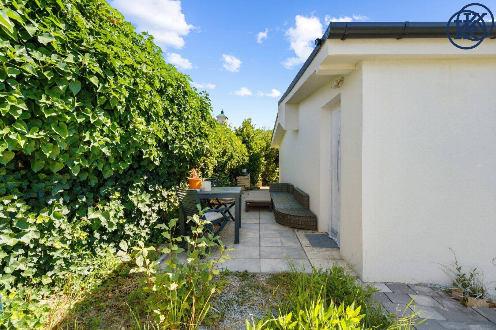 Gemütlicher Terrassenbereich mit Gartenmöbeln, umgeben von einer hohen grünen Hecke.