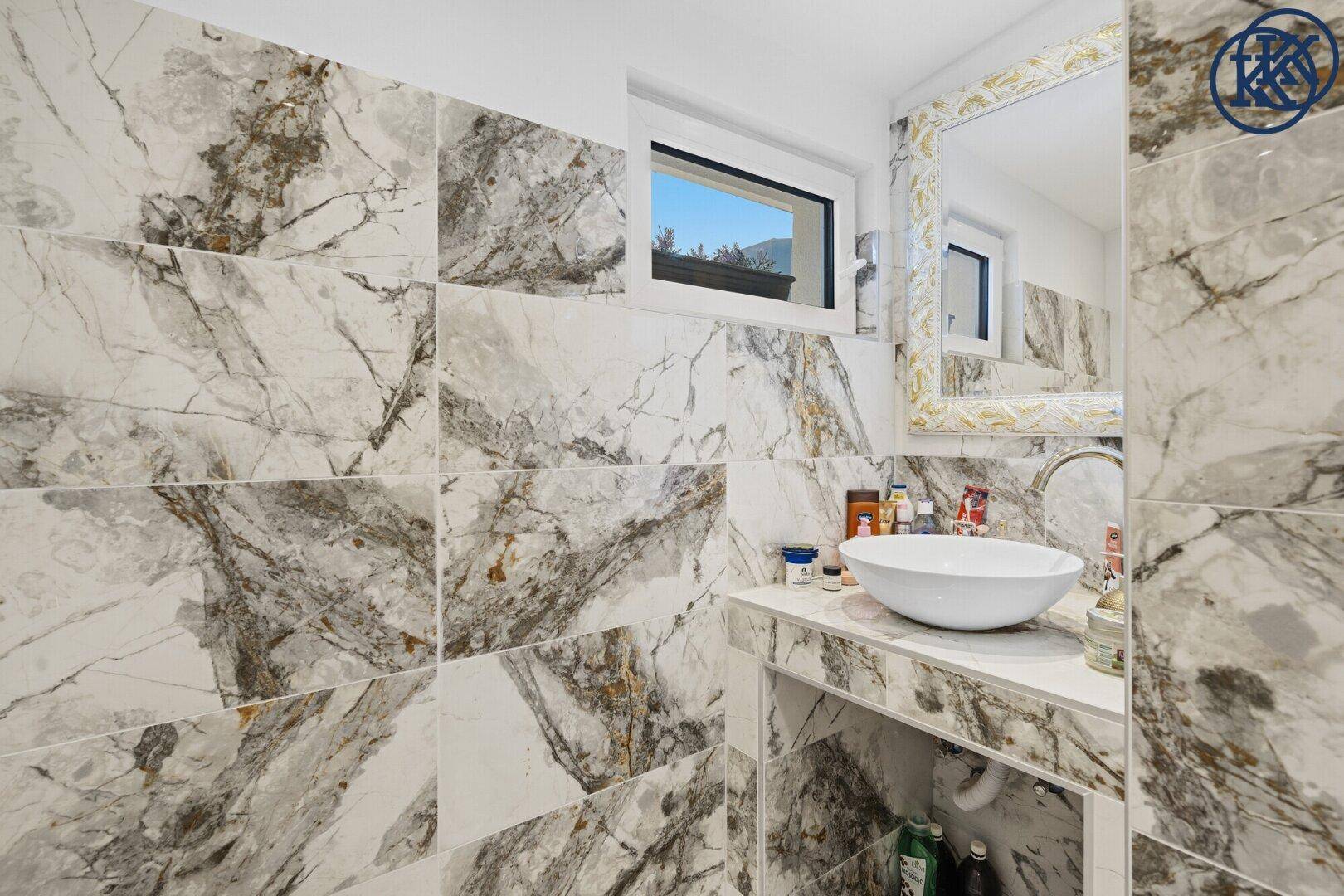 Elegantes Badezimmer mit Marmorfliesen, modernem Waschbecken und Fenster.