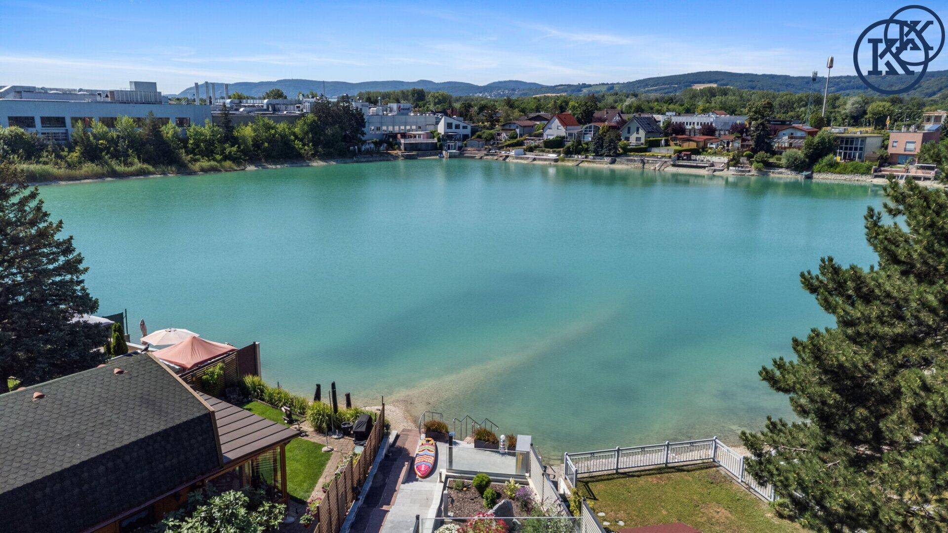 Panoramablick auf den See mit angrenzenden Wohnhäusern und üppiger Vegetation am Ufer.