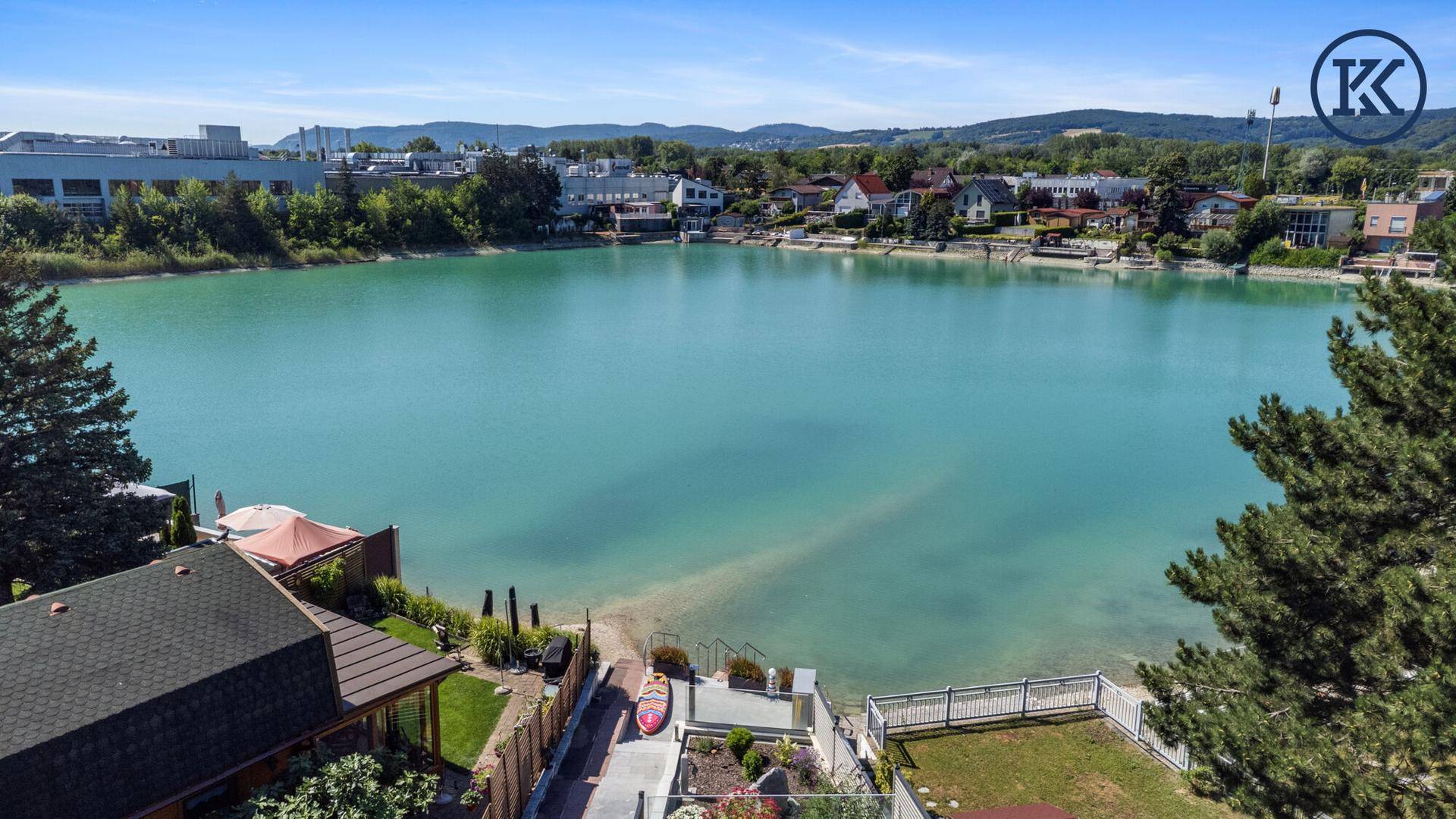 Panoramablick auf den türkisfarbenen See und die angrenzenden Grundstücke mit direktem Seezugang.