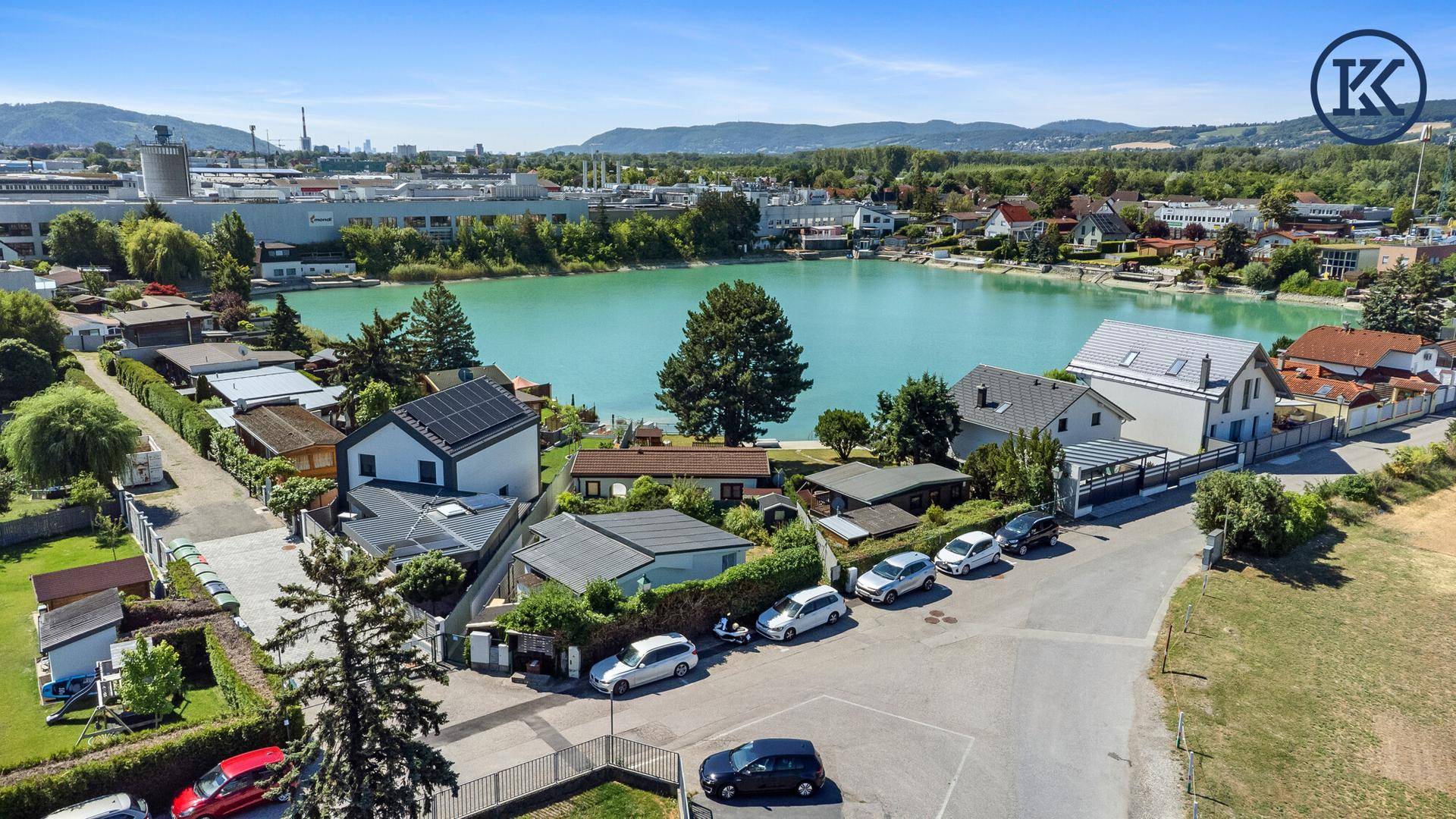 Luftaufnahme der Wohnsiedlung am See mit umliegender Infrastruktur und Bergen im Hintergrund.