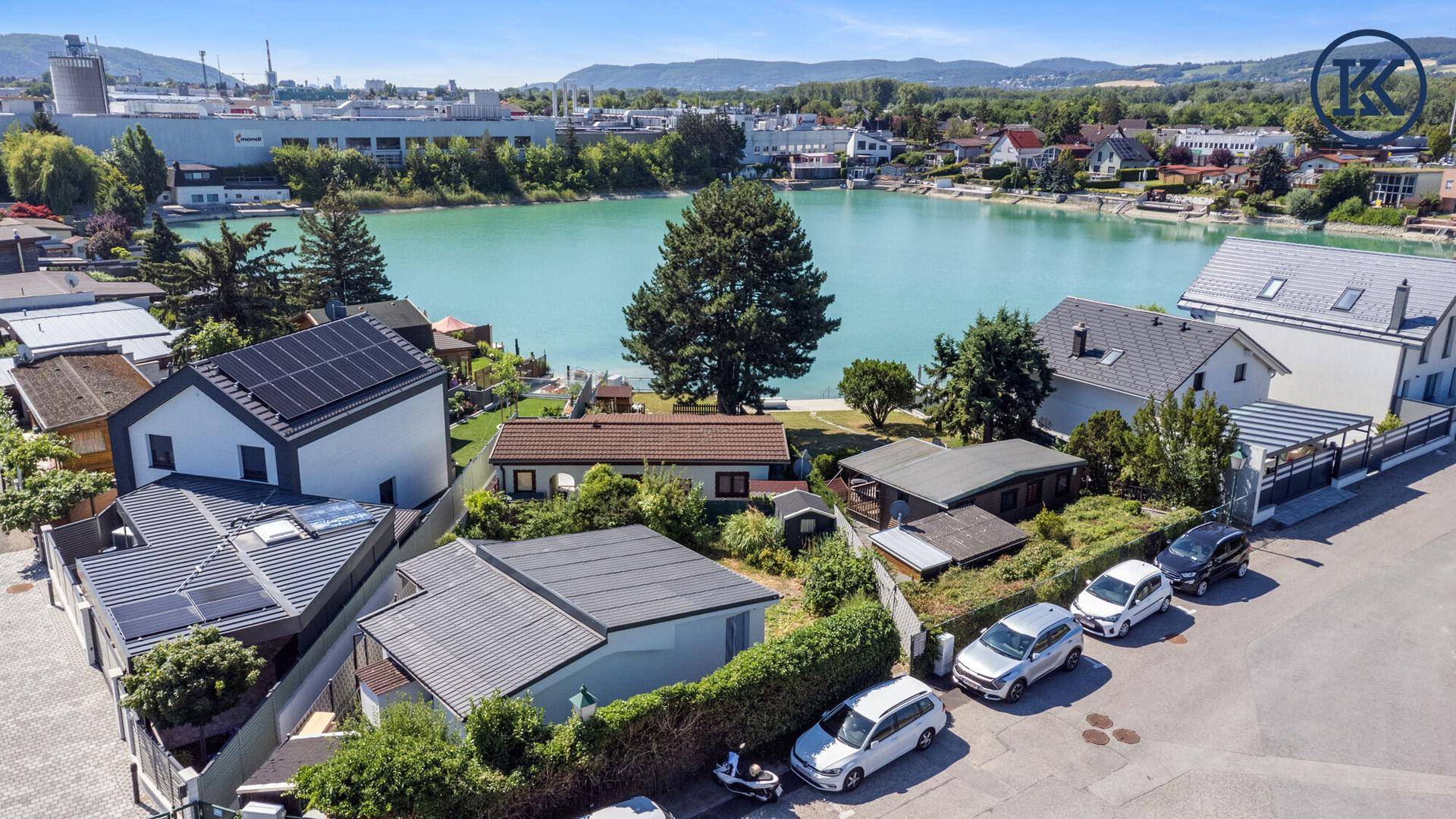 Vogelperspektive auf eine Wohnsiedlung am See mit vielen Bäumen und geparkten Autos.