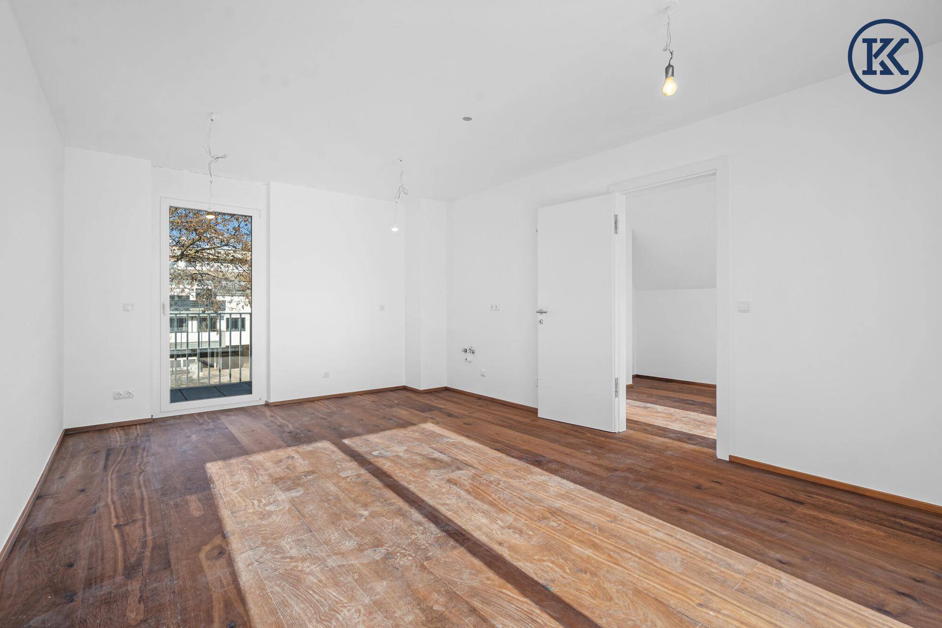 Heller, leerer Raum mit elegantem Holzboden und Zugang zu einem kleinen Balkon.