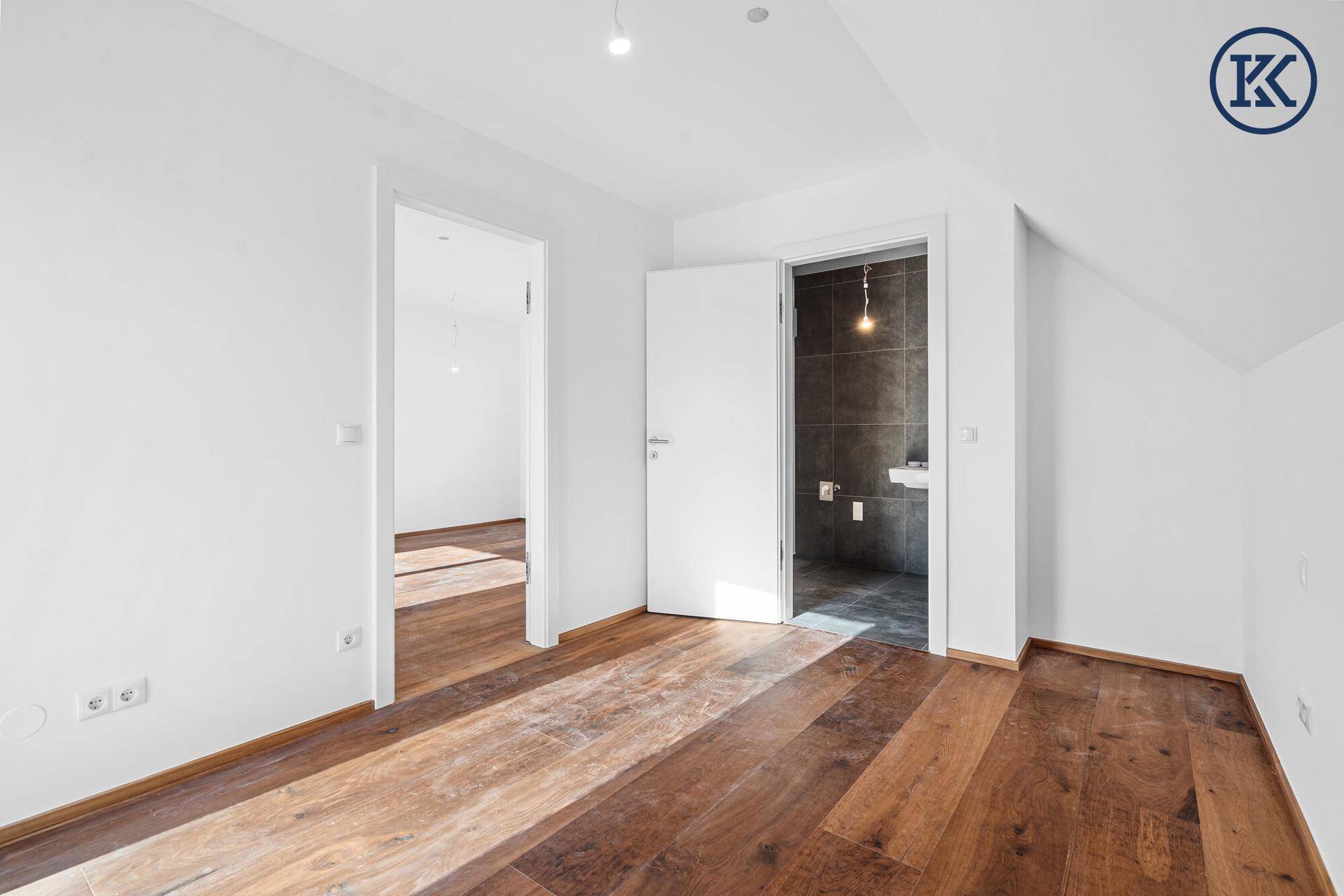 Geräumiges Schlafzimmer mit Holzboden und direktem Zugang zu einem modernen Badezimmer.