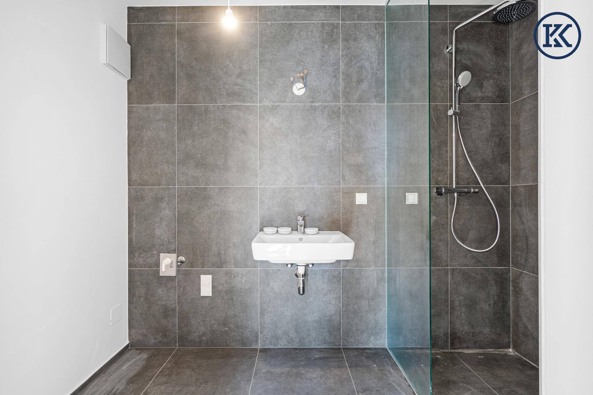 Modernes Badezimmer mit großformatigen grauen Fliesen, Dusche und wandhängendem Waschbecken.