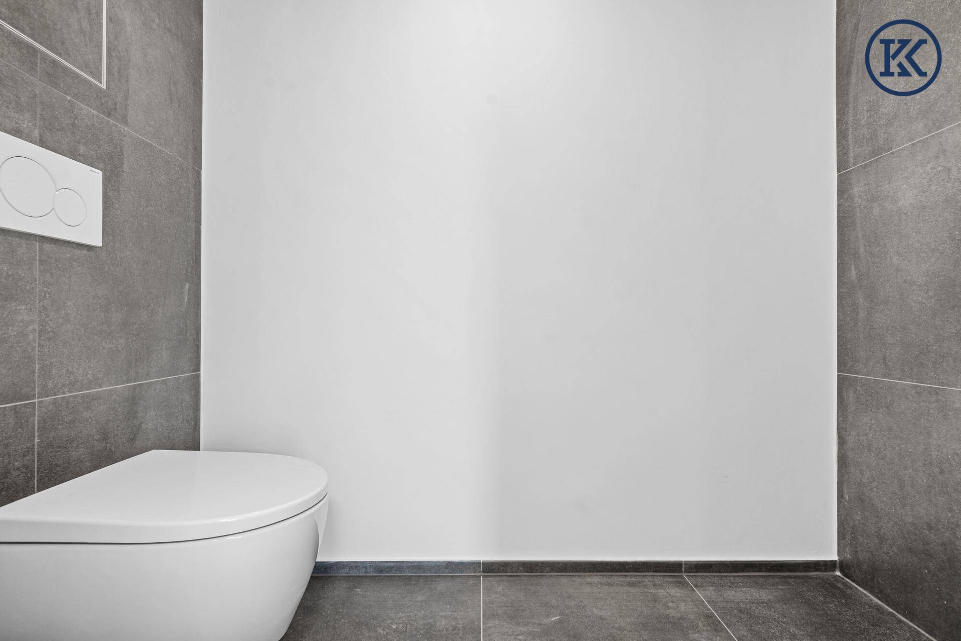 Modernes WC mit wandhängender Toilette und großformatigen grauen Wand- und Bodenfliesen.