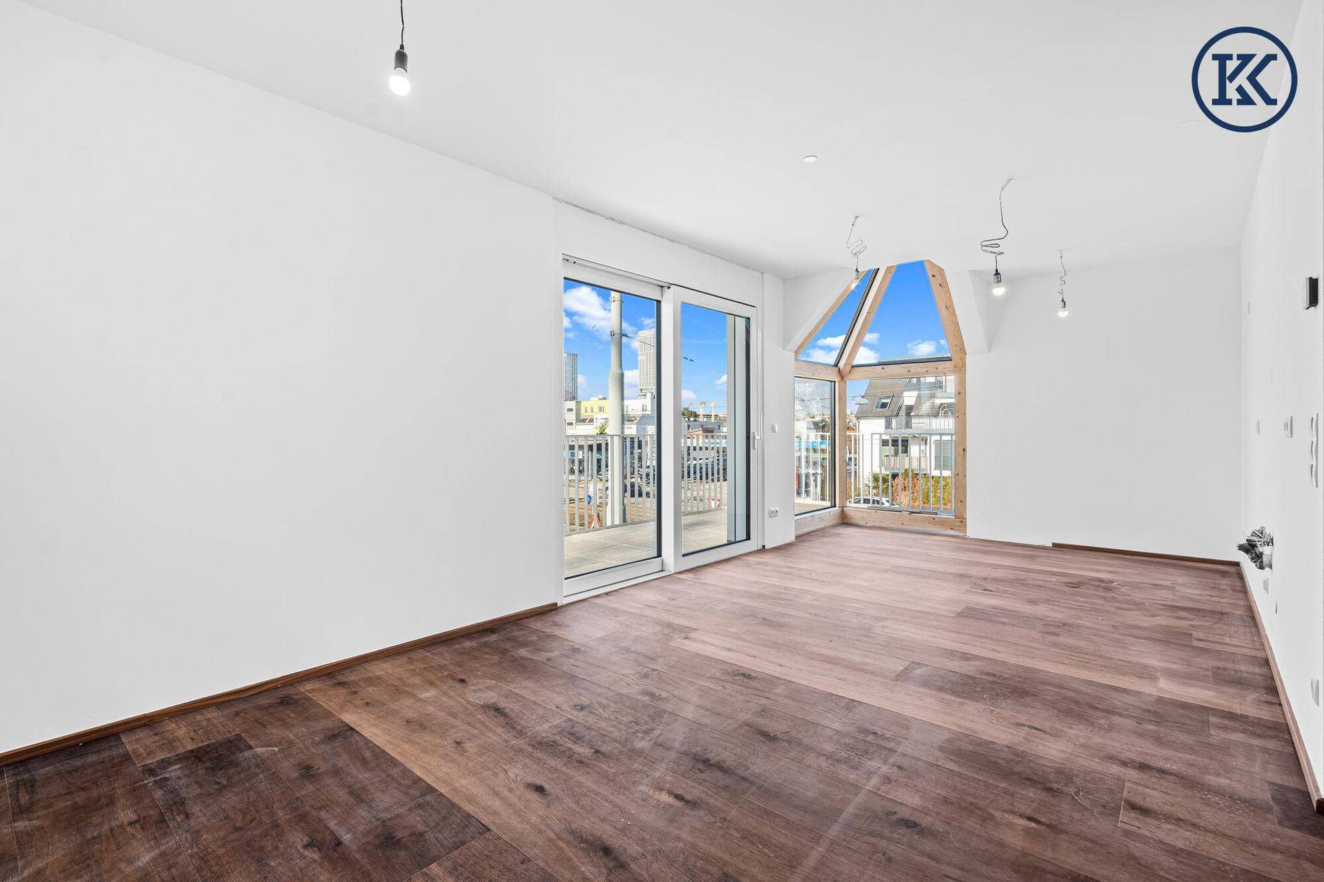 Heller Wohnbereich mit dunklem Holzboden, großen Schiebetüren zum Balkon und einzigartigem Giebelfenster.