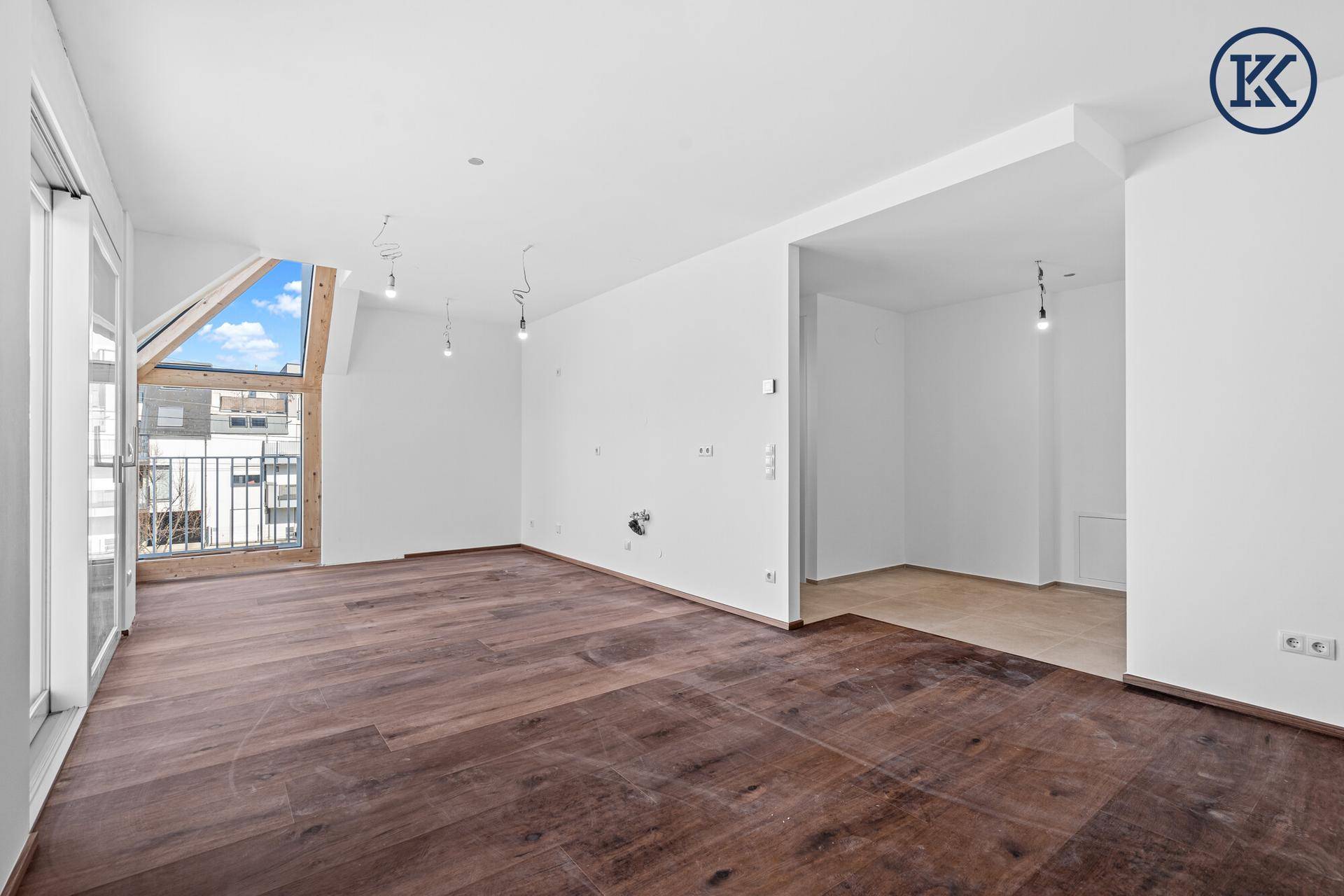 Geräumiger Wohnbereich mit dunklem Holzboden, weißen Wänden und einem markanten Giebelfenster.