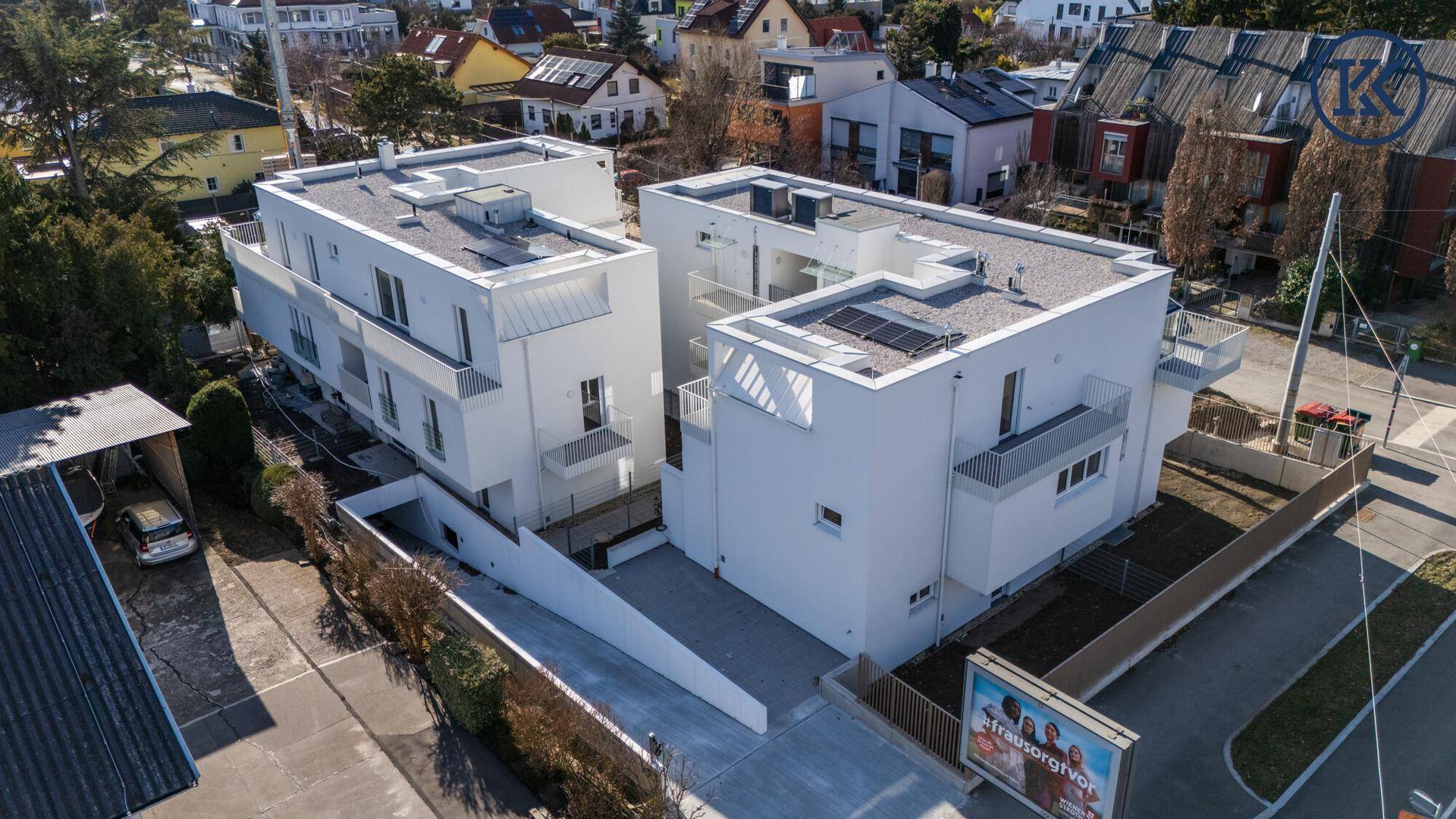 Vogelperspektive auf den modernen Neubau mit weißer Fassade und umliegender Wohnbebauung.