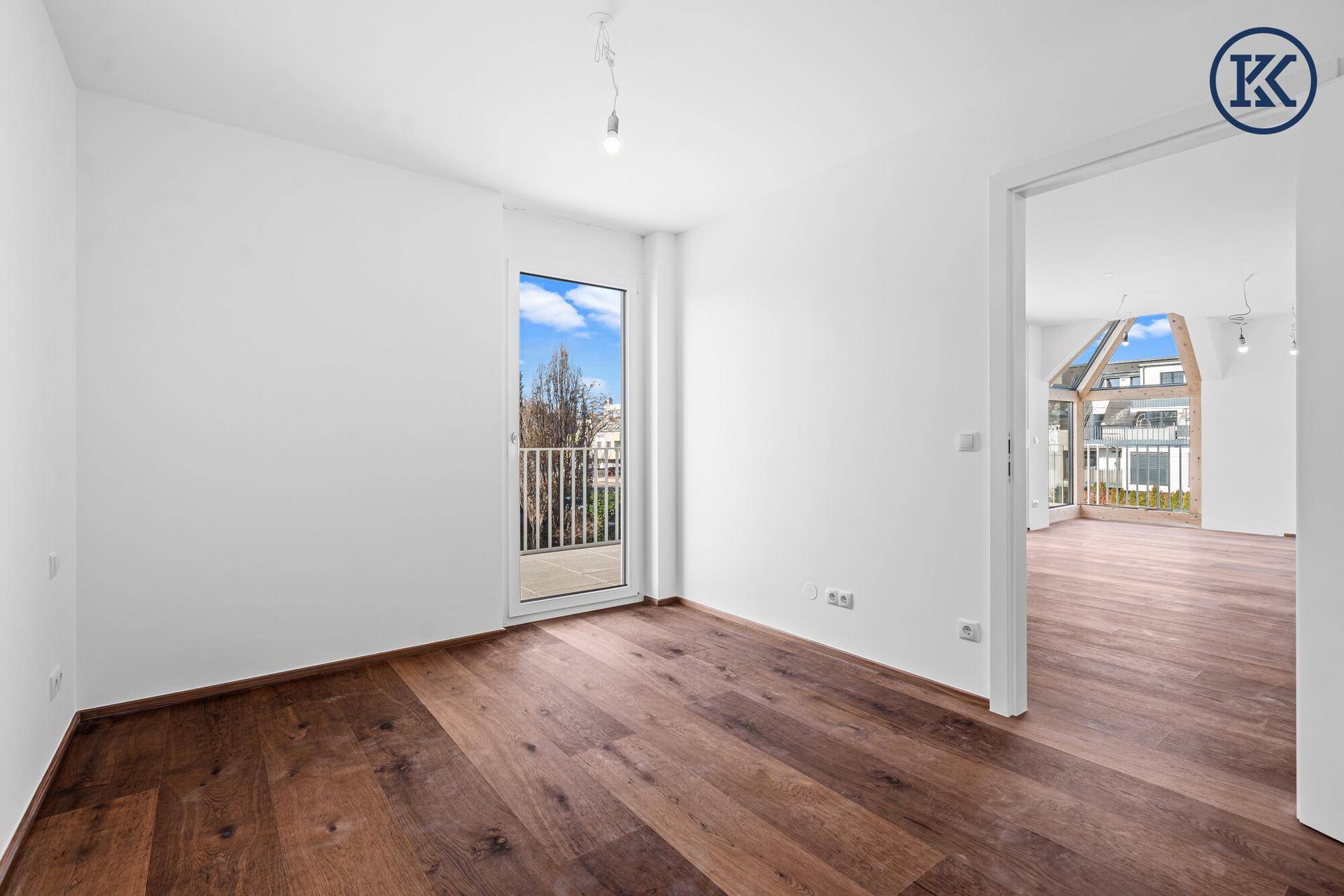 Helles Zimmer mit dunklem Holzboden und Zugang zu einem französischen Balkon.