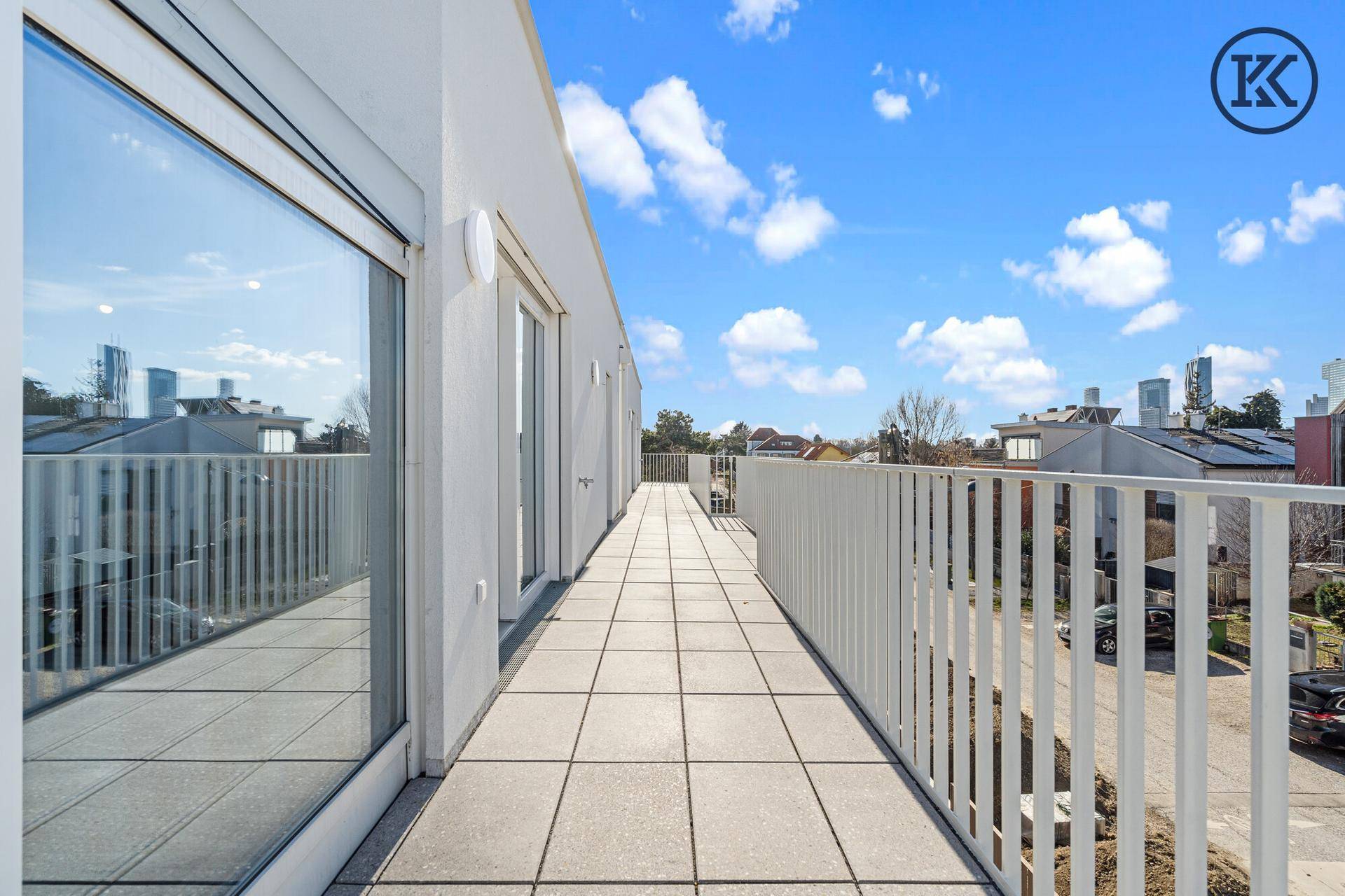 Langer Balkon mit Fliesenboden und weißem Geländer, bietet einen weiten Blick auf die Stadt.