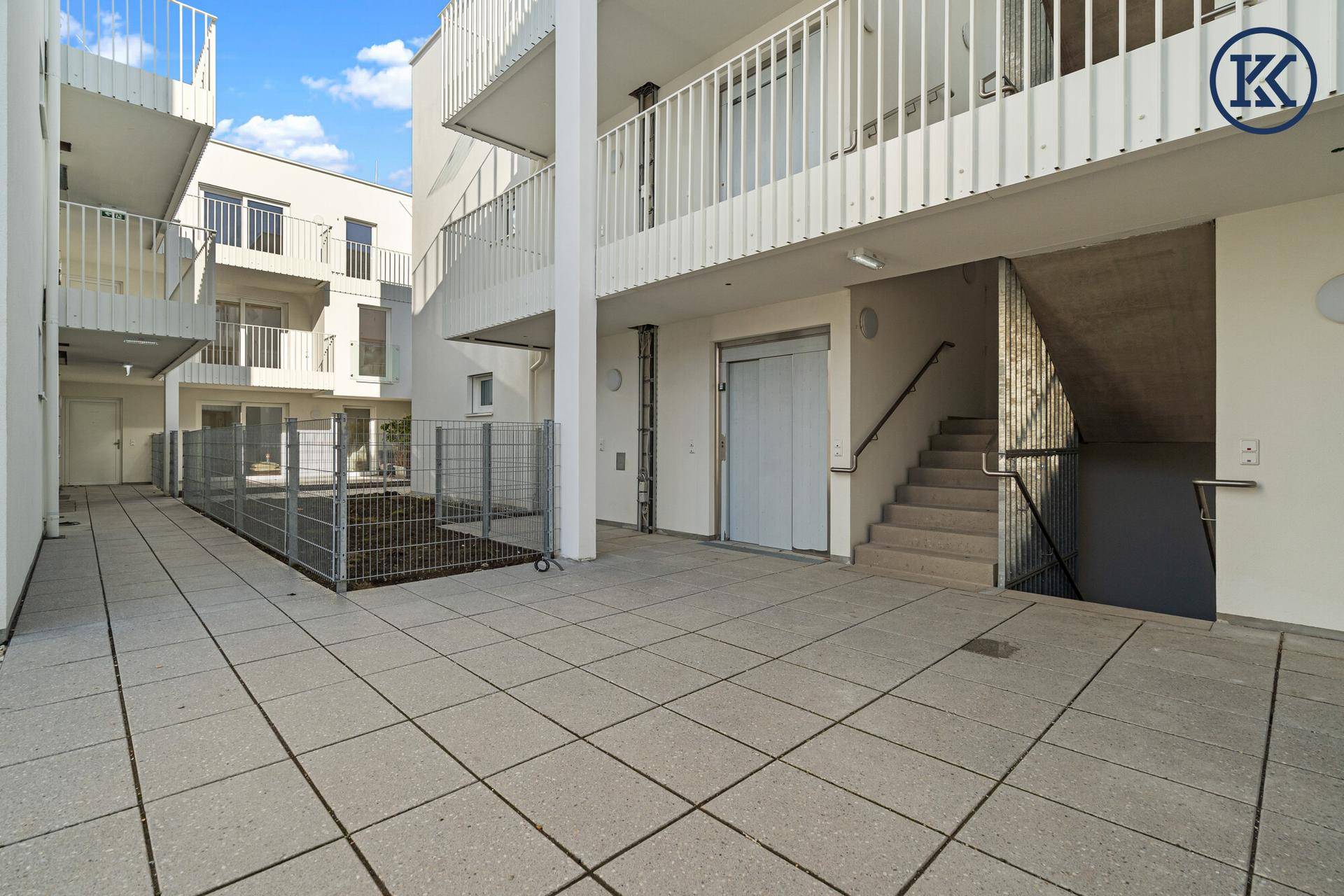 Außenbereich mit Fliesenboden, Treppenhaus und einem Aufzug, der die Etagen verbindet.