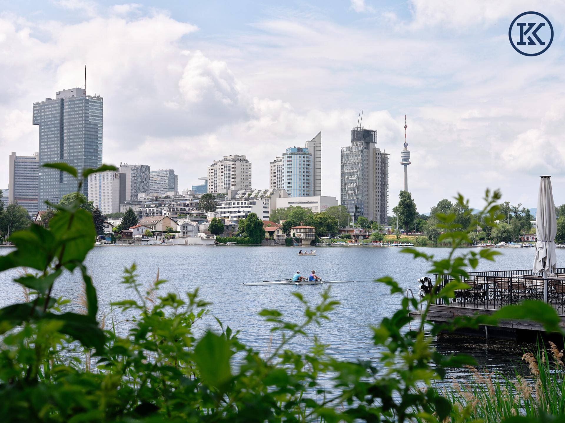Idyllischer Seeblick mit Ruderbooten und der markanten Wiener Skyline am Horizont.