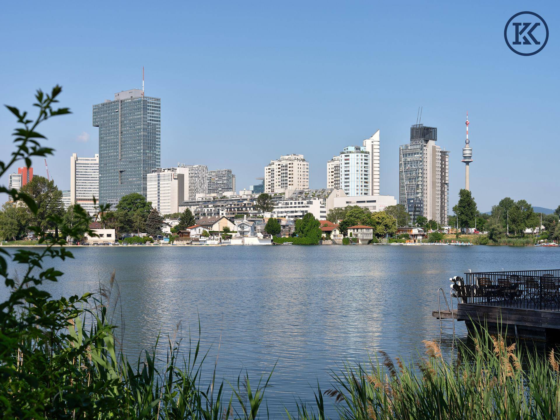 Klarer Seeblick auf die Wiener Skyline an einem sonnigen Tag, umgeben von üppigem Grün.