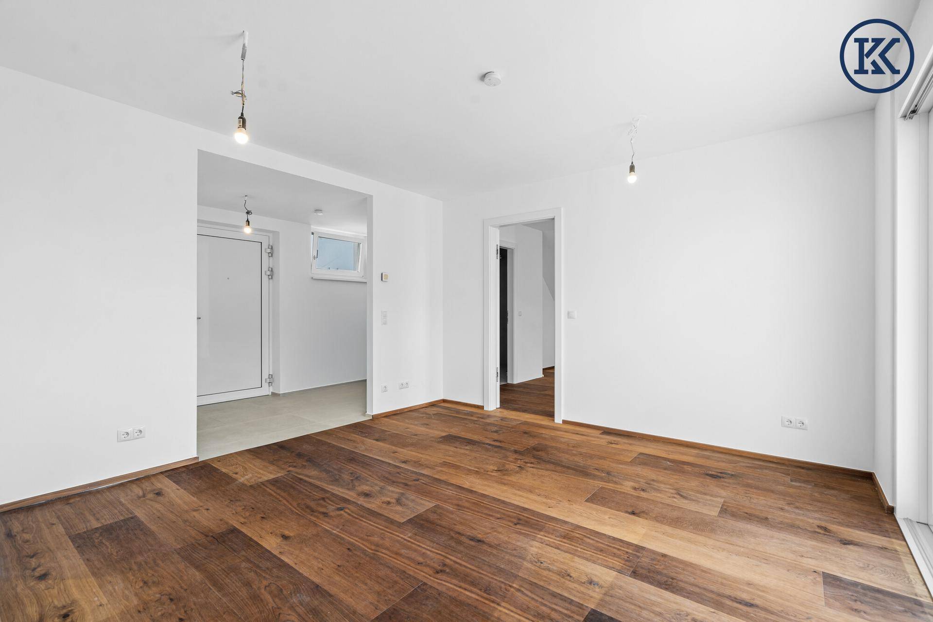 Heller Wohnraum mit Holzboden, weißen Wänden und Blick auf den Eingangsbereich und ein weiteres Zimmer.