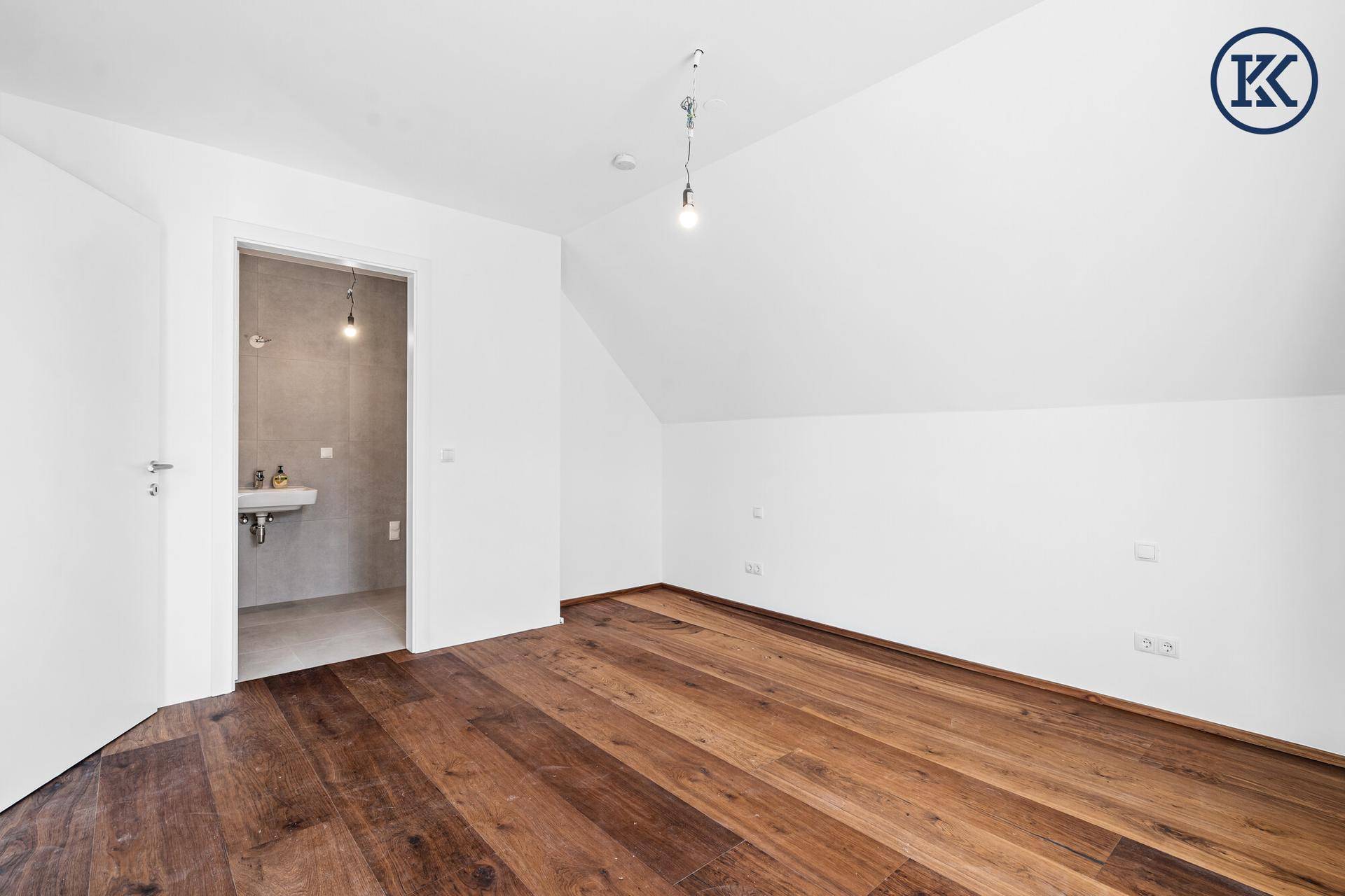 Schlafzimmer mit Holzboden und Dachschräge, das direkt mit einem modernen Badezimmer verbunden ist.