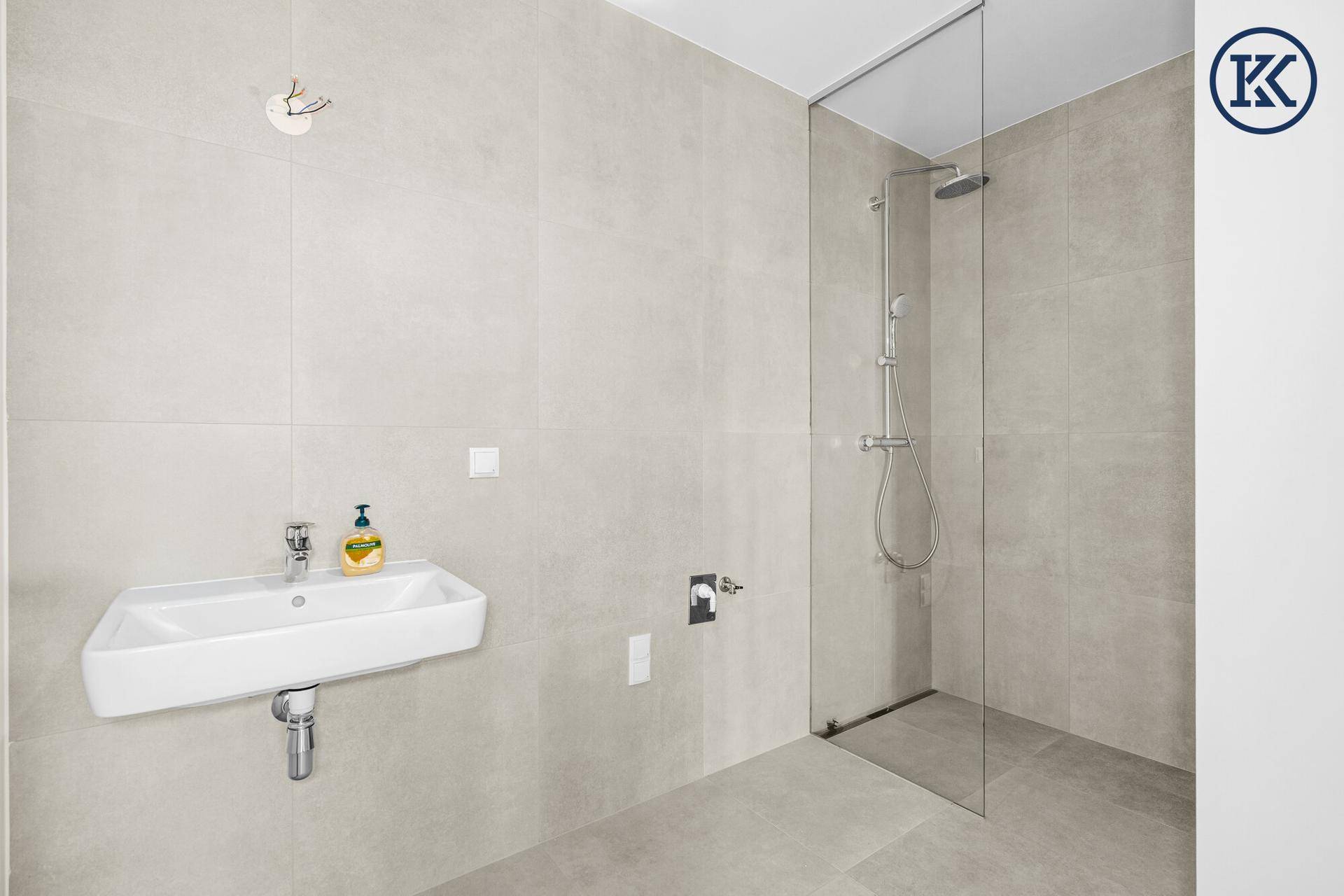 Modernes Badezimmer mit wandhängendem Waschbecken, begehbarer Dusche und hellgrauen Fliesen.