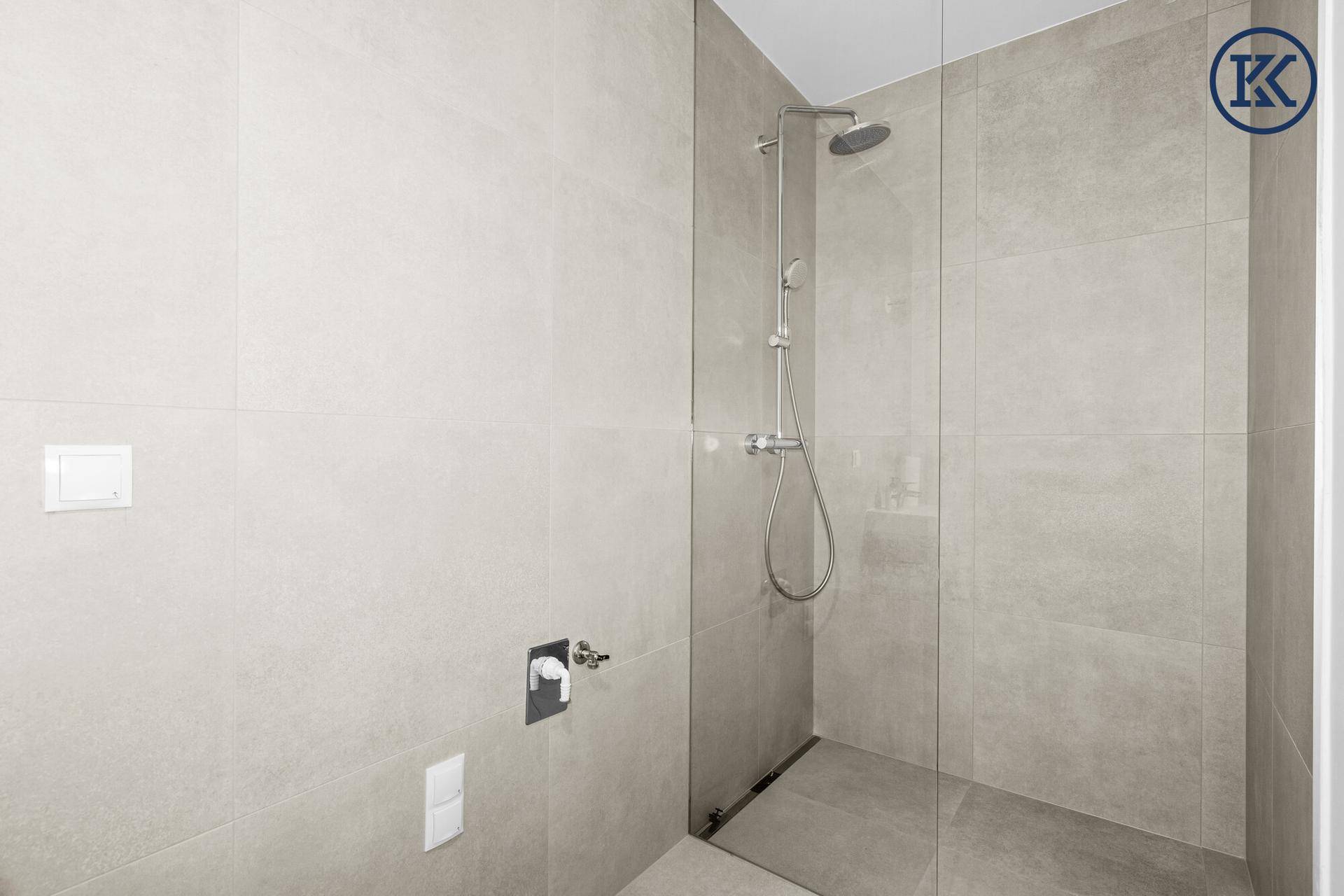 Moderne begehbare Dusche mit Glaswand und großformatigen hellgrauen Fliesen.