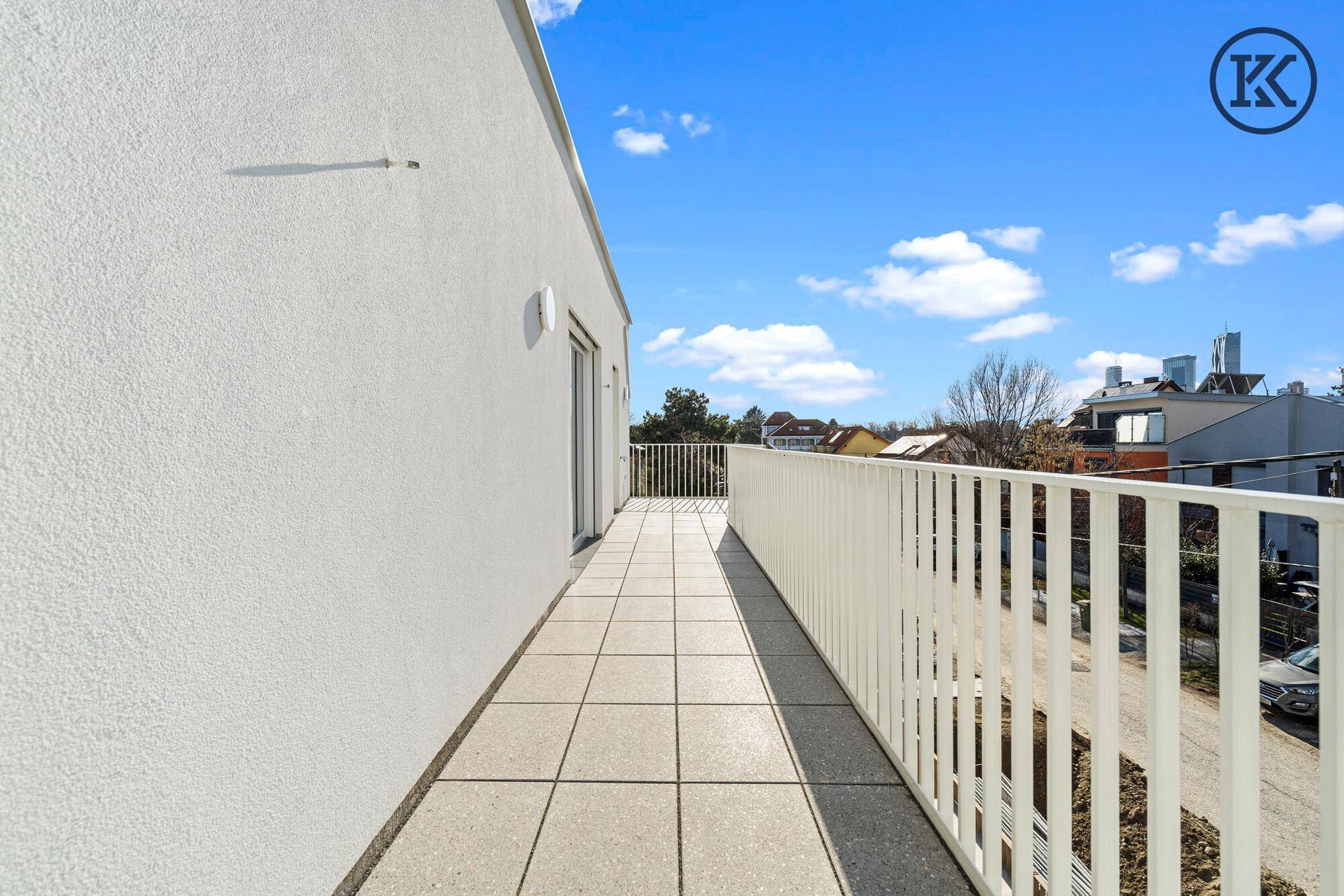 Langer, sonniger Balkon mit Fliesenboden und weißem Geländer, ideal für Entspannung im Freien.