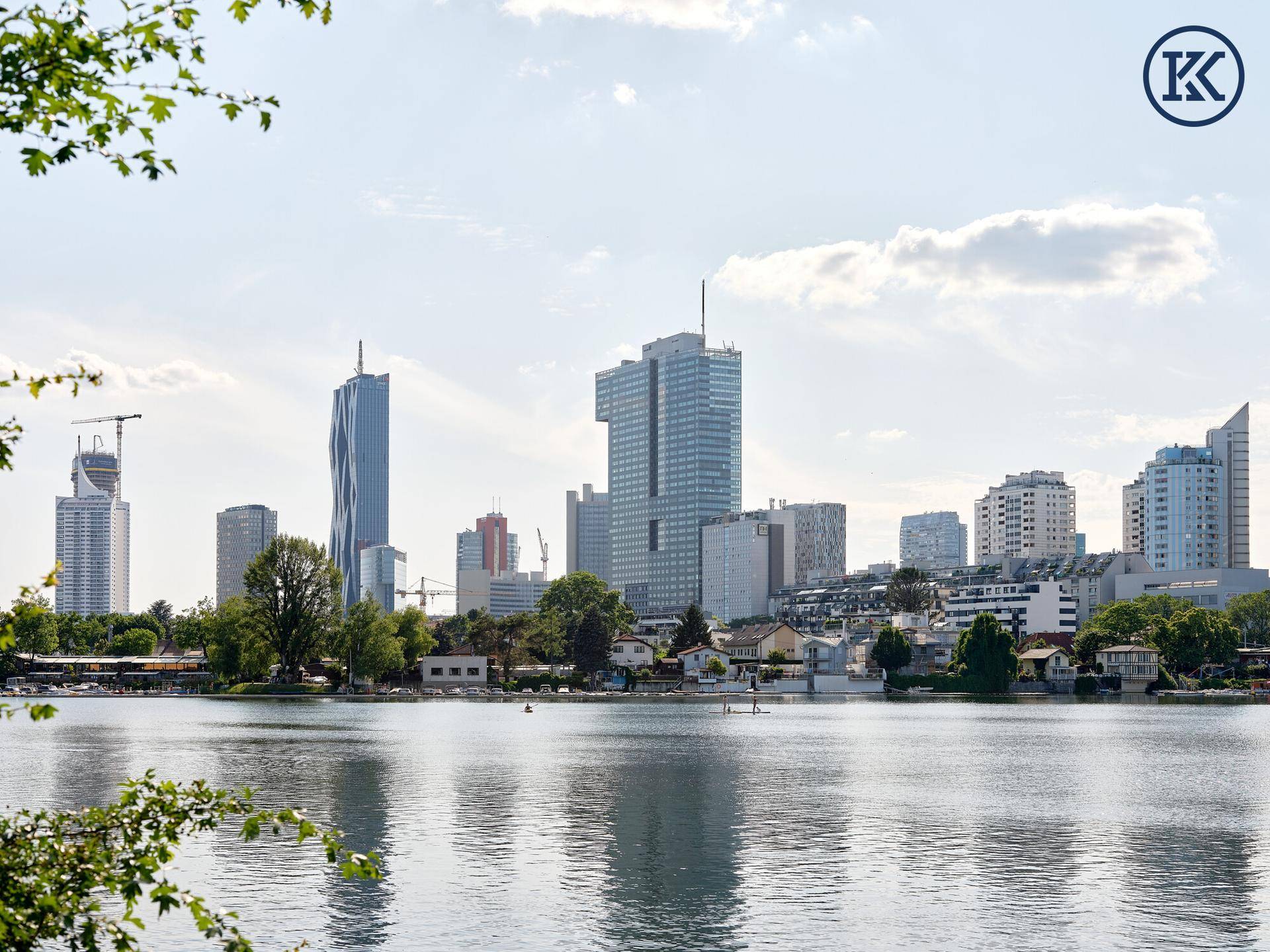 Skyline der Donau City vom Wasser aus gesehen, umgeben von grünen Ufern und klarem Himmel.