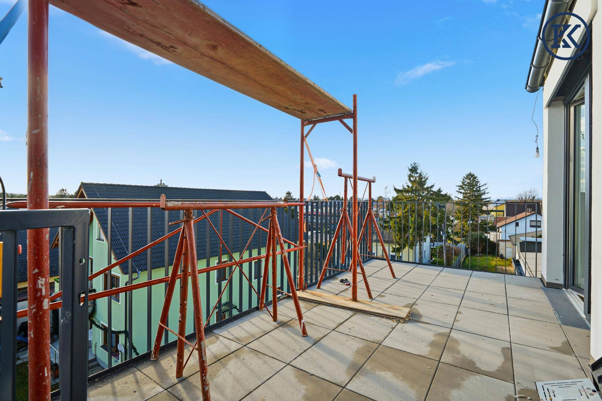 Terrasse im Bau mit Metallgeländer und weitem Blick über die Dächer der umliegenden Häuser.