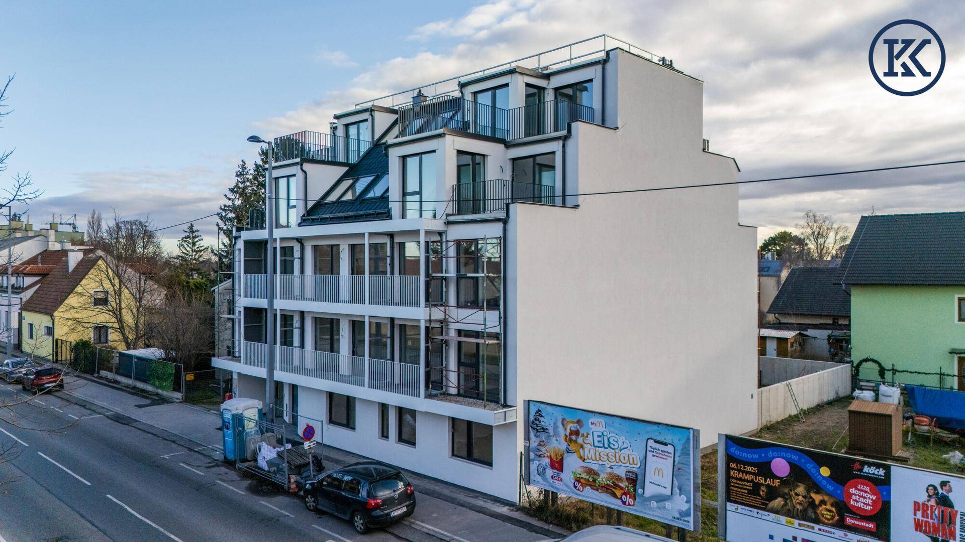 Modernes Wohngebäude an einer Straße mit Balkonen und großen Fenstern, umgeben von städtischer Bebauung.