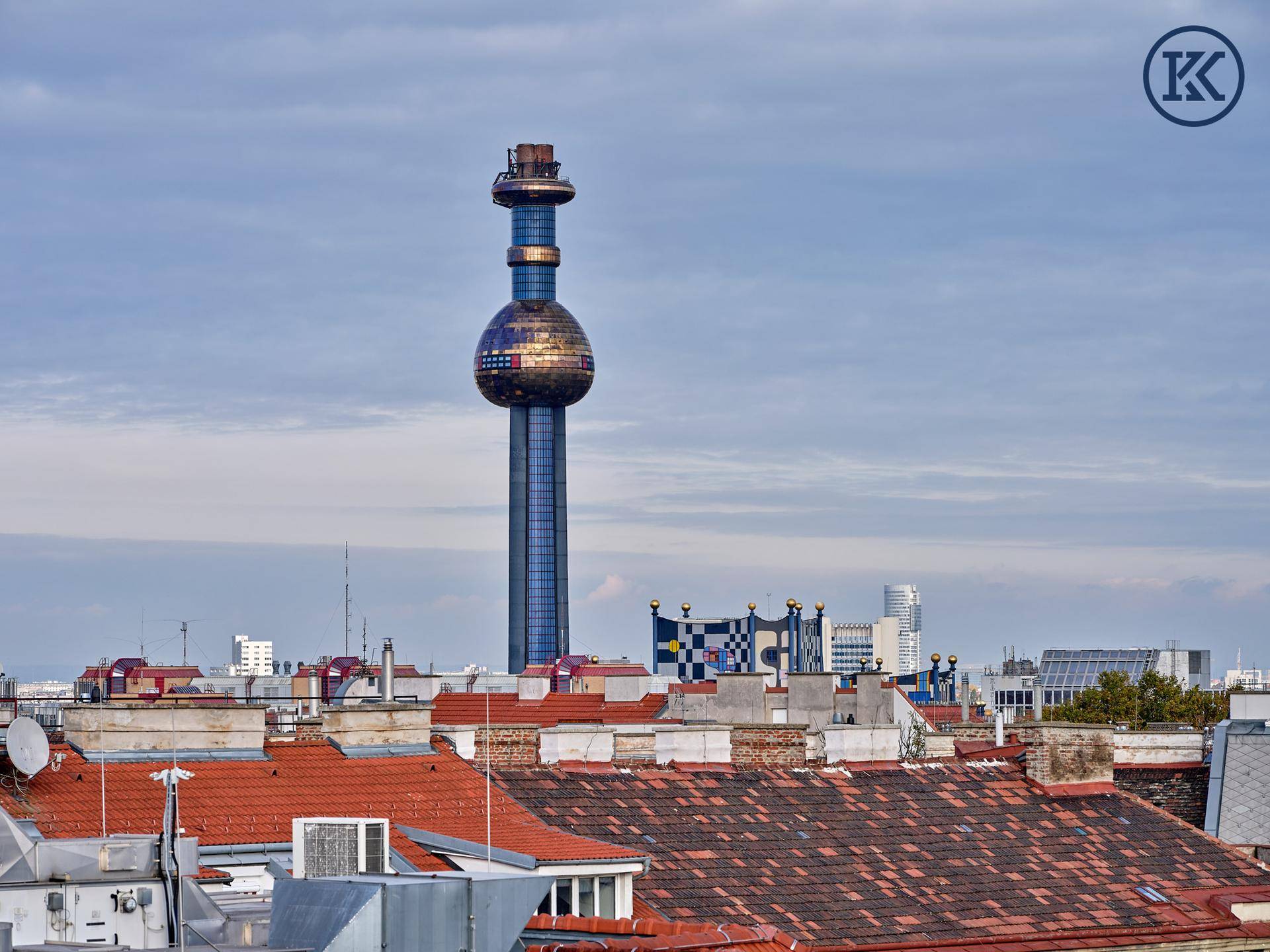 Weitläufiger Stadtblick mit einem markanten Fernsehturm und umliegenden Dächern unter blauem Himmel.