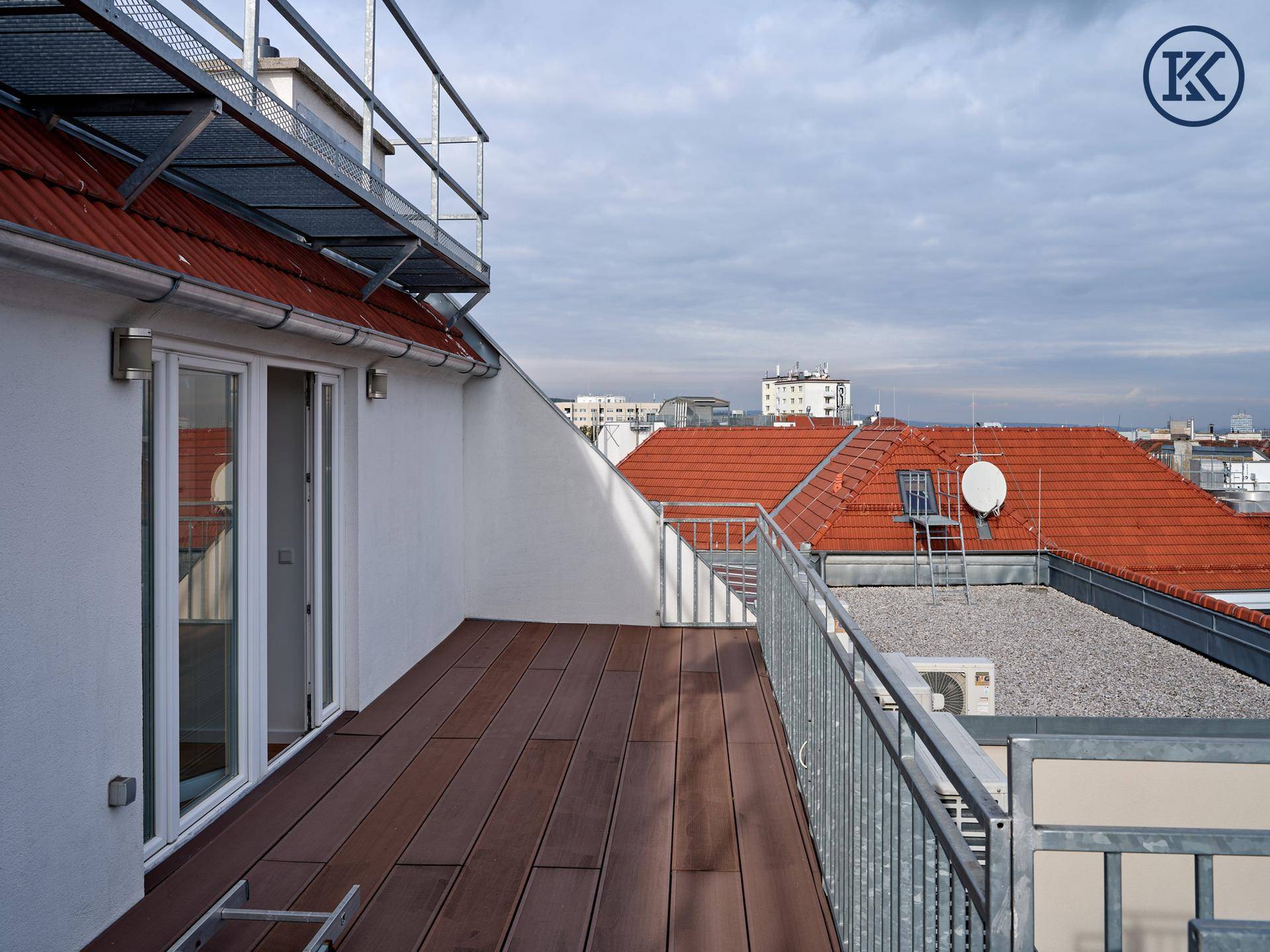 Dachterrasse mit Holzdielen und Zugang zu einem Innenraum, umgeben von Dächern.