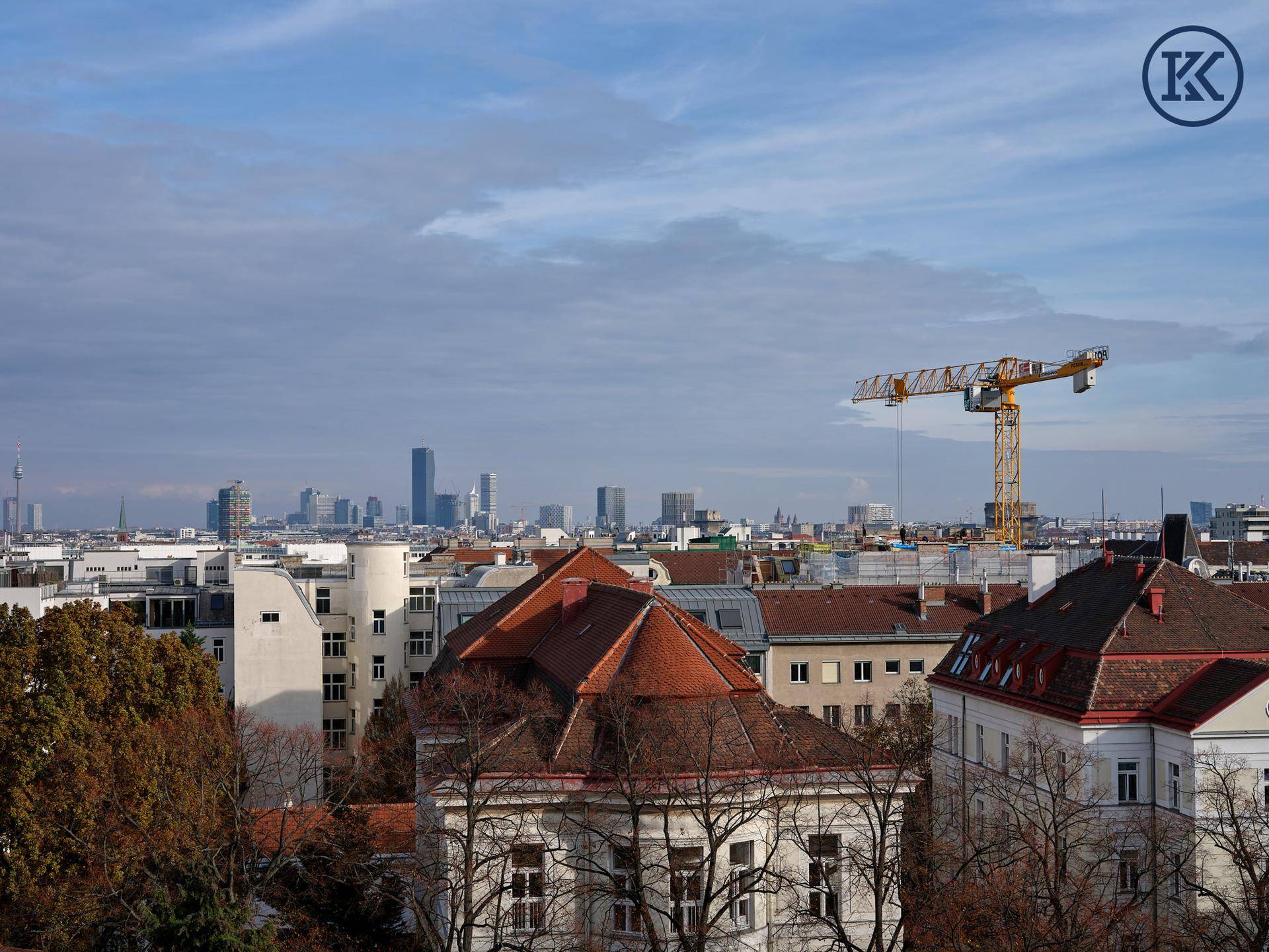 Weitläufiger Stadtblick mit Hochhäusern, einem Baukran und traditionellen Dächern unter bewölktem Himmel.