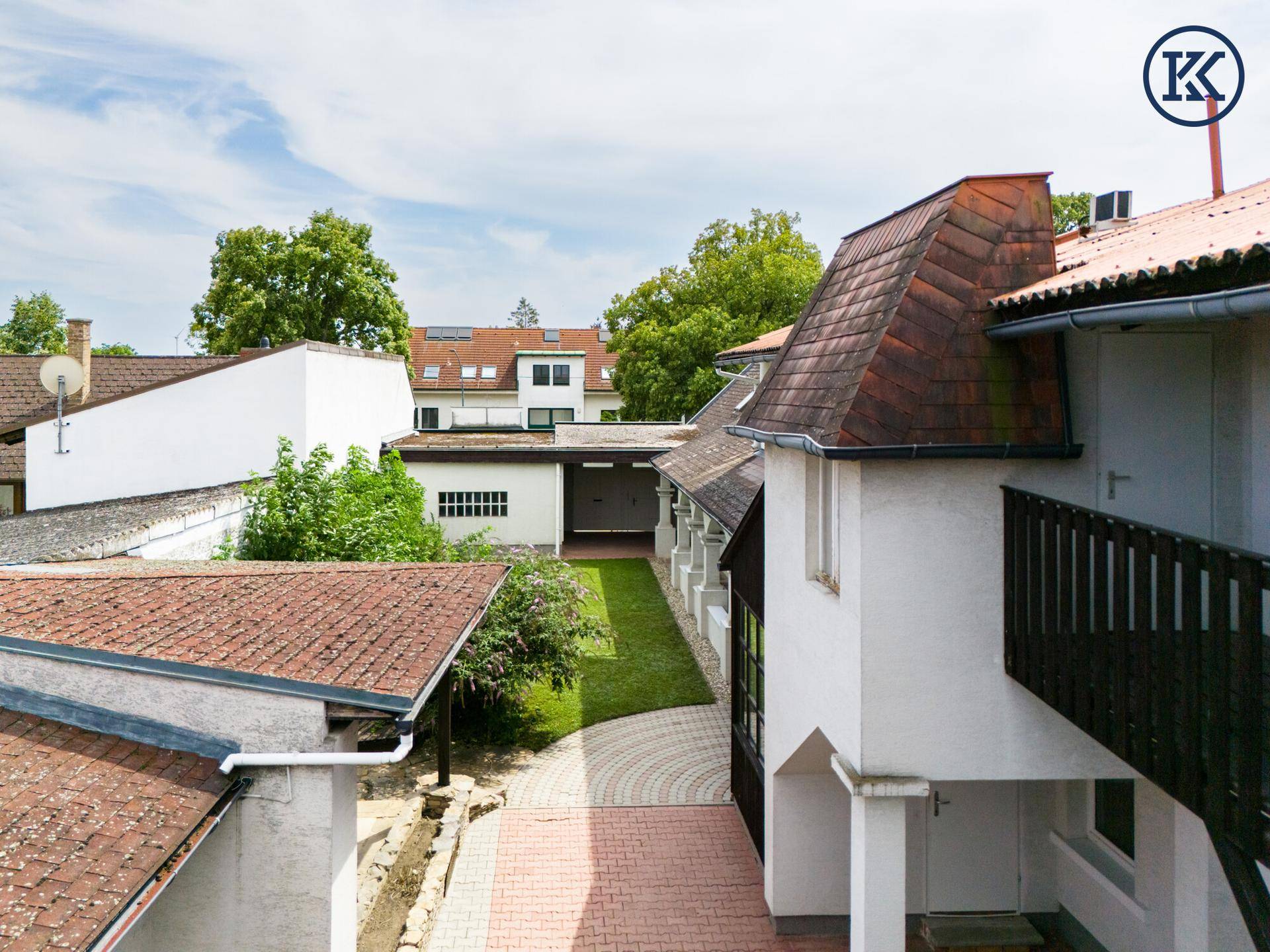 Blick auf den Innenhof mit gepflastertem Weg, Grünflächen und angrenzenden Gebäuden unter blauem Himmel.