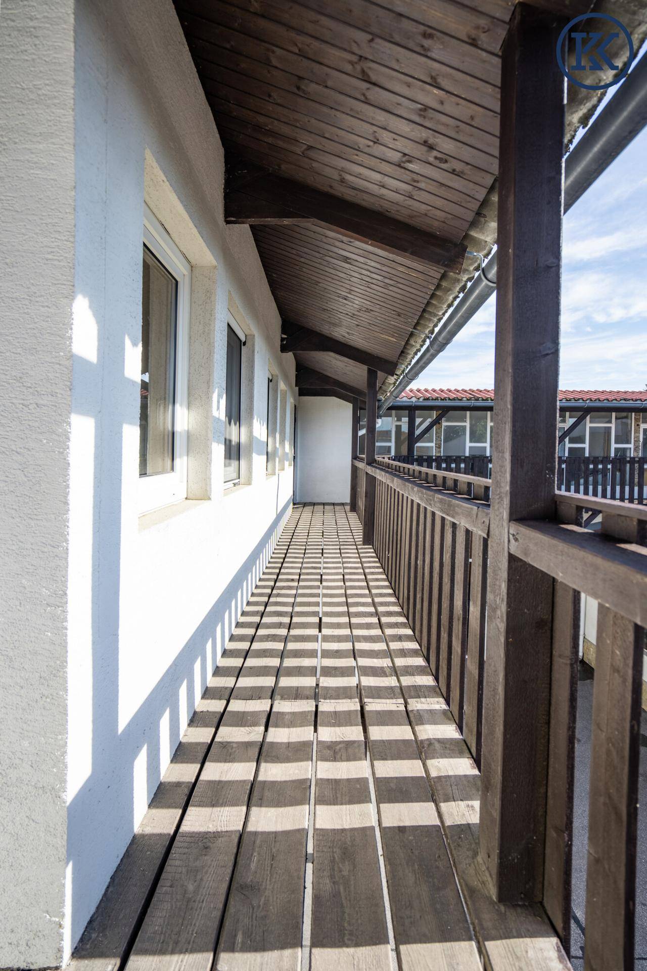 Langer, schmaler Holzbalkon mit Geländer und überdachtem Bereich, ideal zum Entspannen.