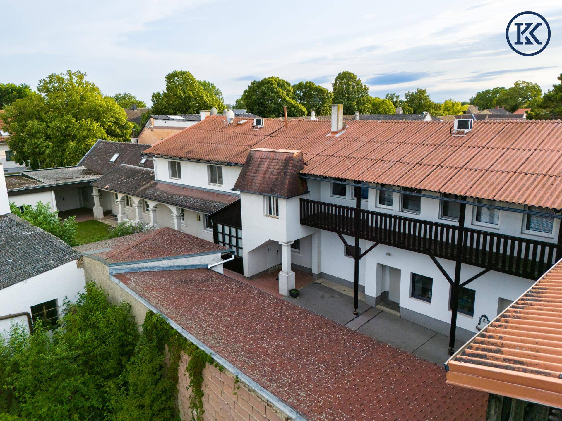 Luftaufnahme des weitläufigen Innenhofs mit mehreren Gebäuden und einem langen Holzbalkon.