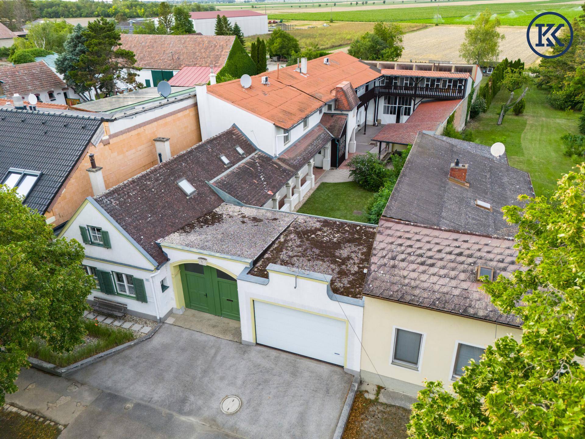 Luftaufnahme des Anwesens mit Hauptgebäude, Garage und Innenhof, umgeben von Feldern.
