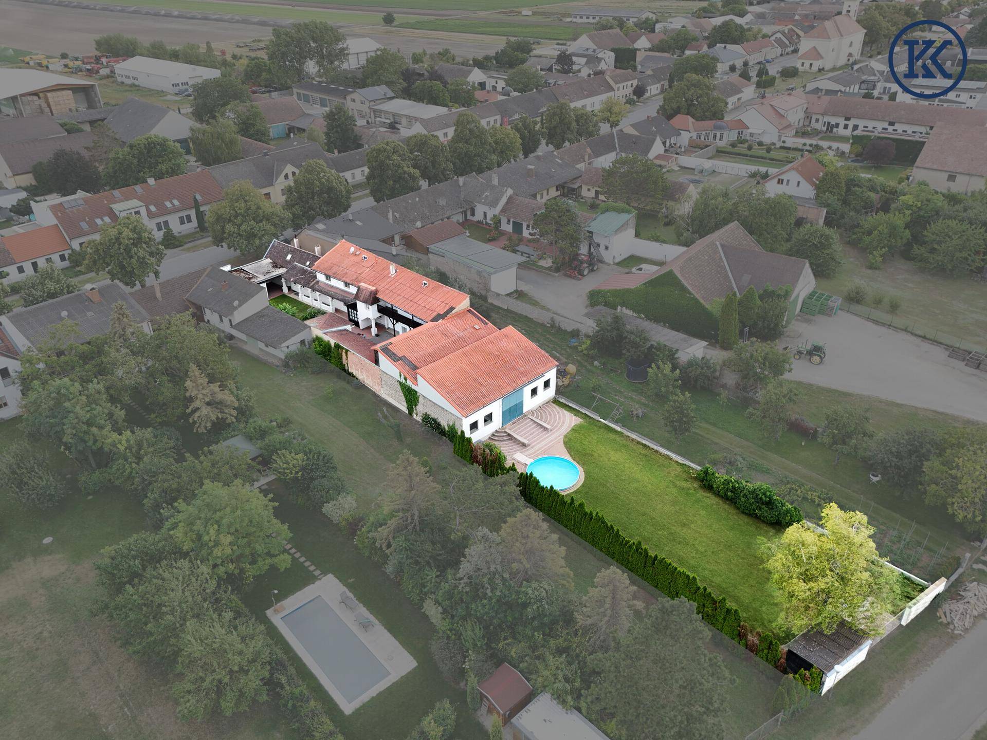 Luftaufnahme des Anwesens mit Hauptgebäude, langem Garten, Pool und umliegenden Häusern.