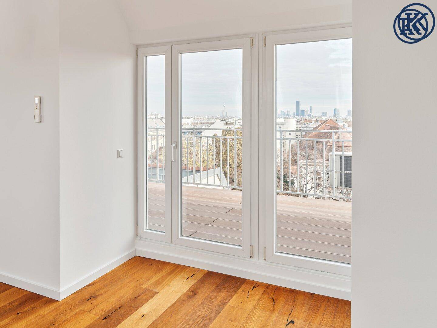 Helles Zimmer mit Holzboden und großen Glasfenstern, die Zugang zu einer Terrasse mit Stadtblick bieten.