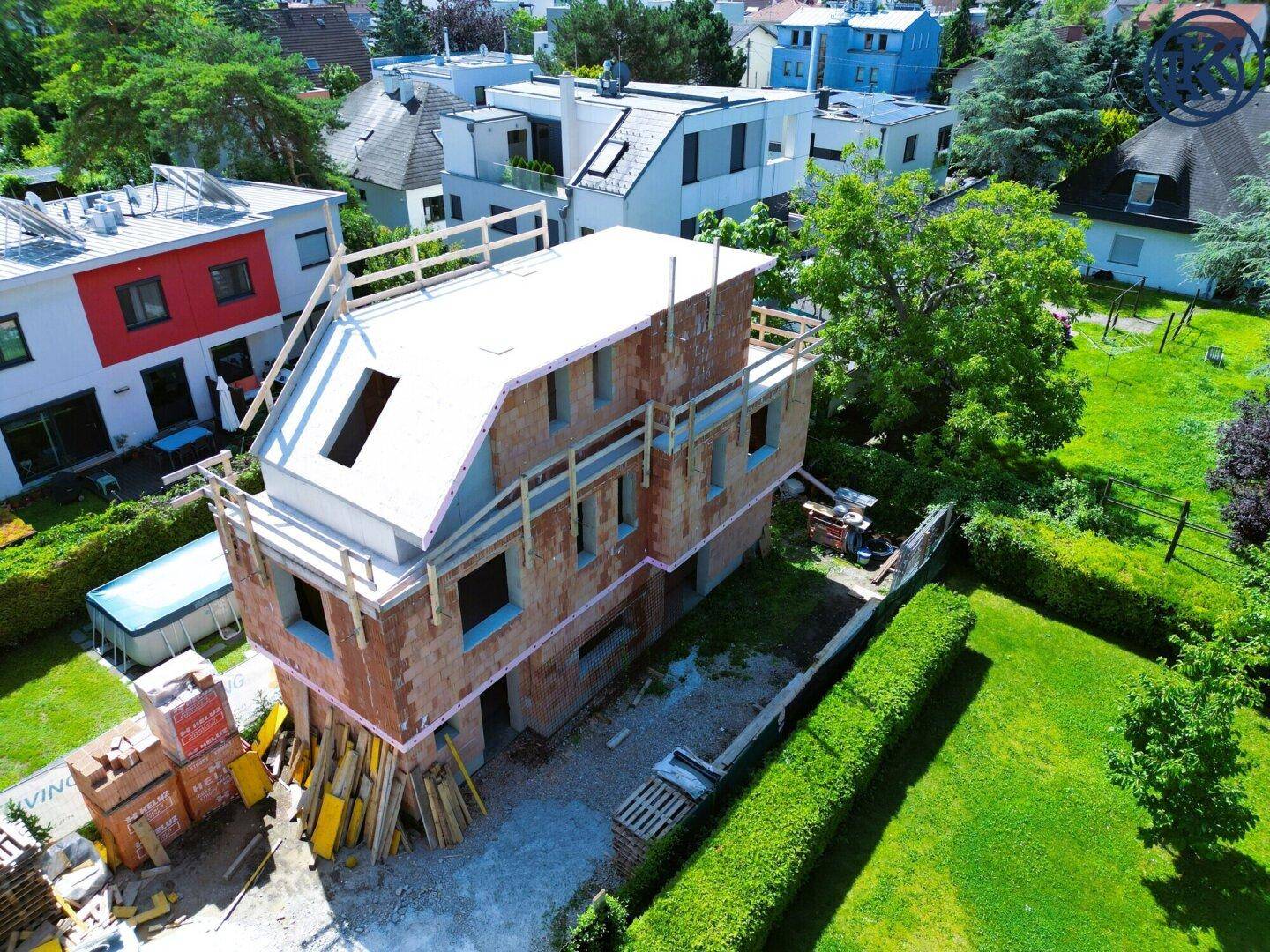 Haus im Rohbau mit Dachkonstruktion und Baumaterialien auf dem Grundstück in Wohngegend.