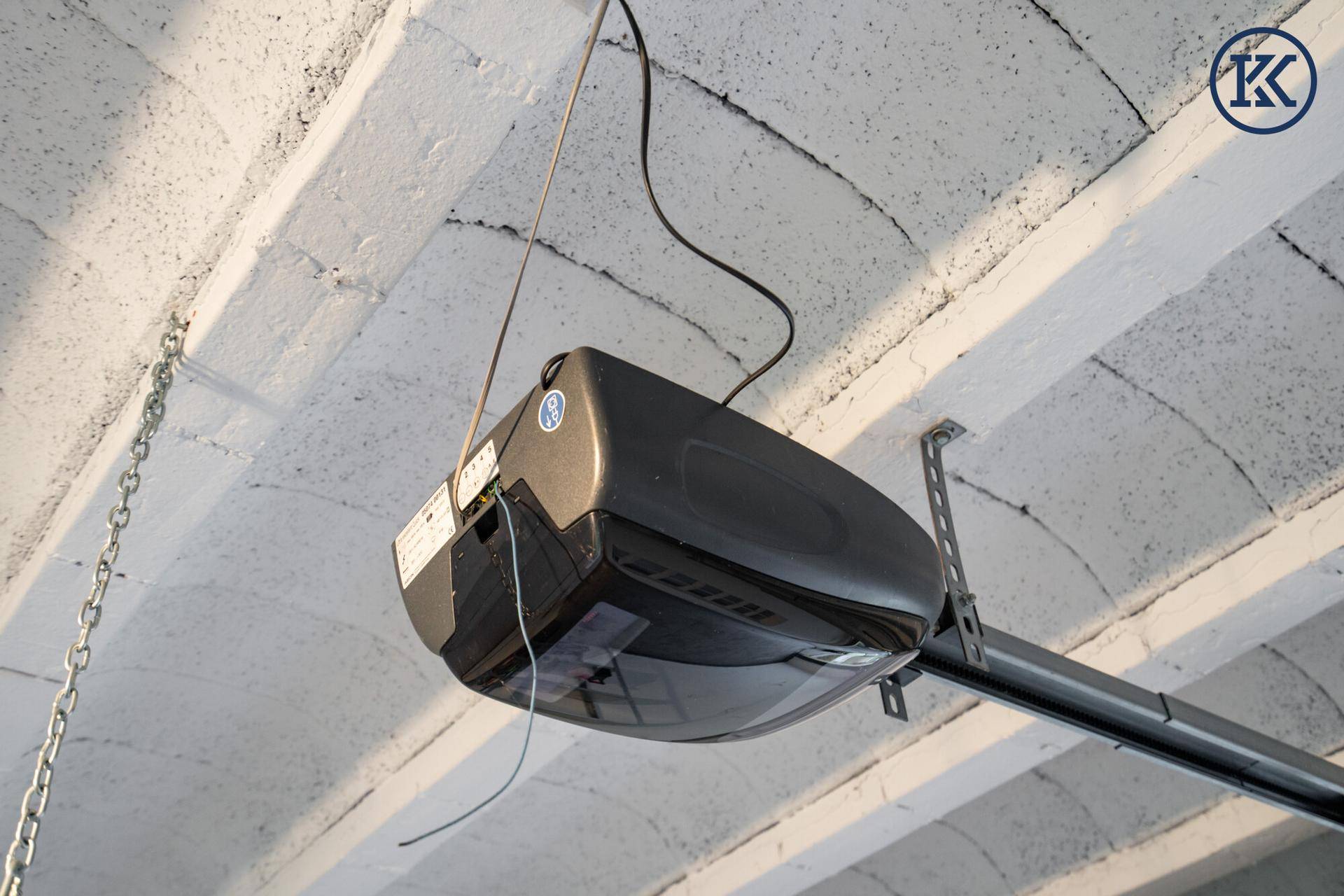 Detailaufnahme des automatischen Garagentoröffners an der Decke mit sichtbaren Kabeln.