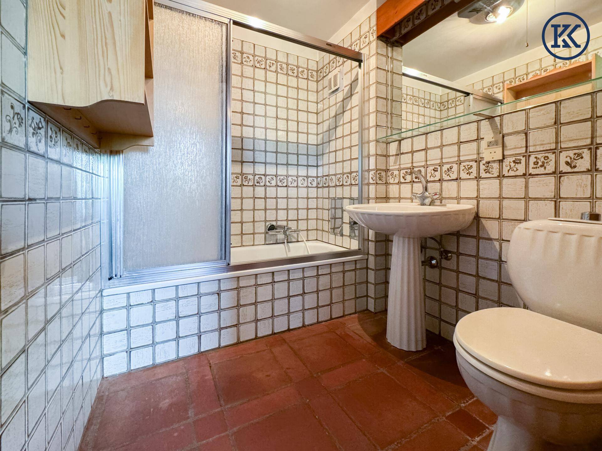 Badezimmer mit traditionellen Fliesen, Badewanne mit Duschabtrennung und Standwaschbecken.