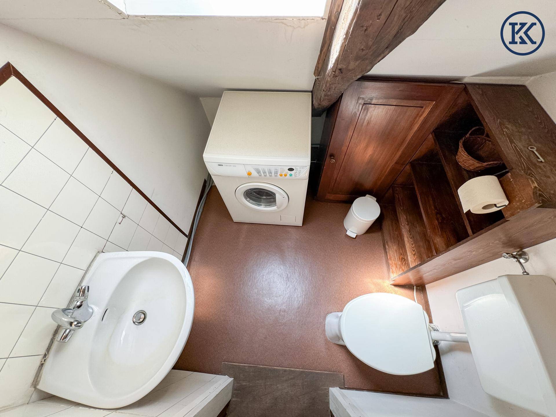 Kleiner Raum mit Toilette, Waschbecken und Waschmaschine, unter einer Dachschräge gelegen.