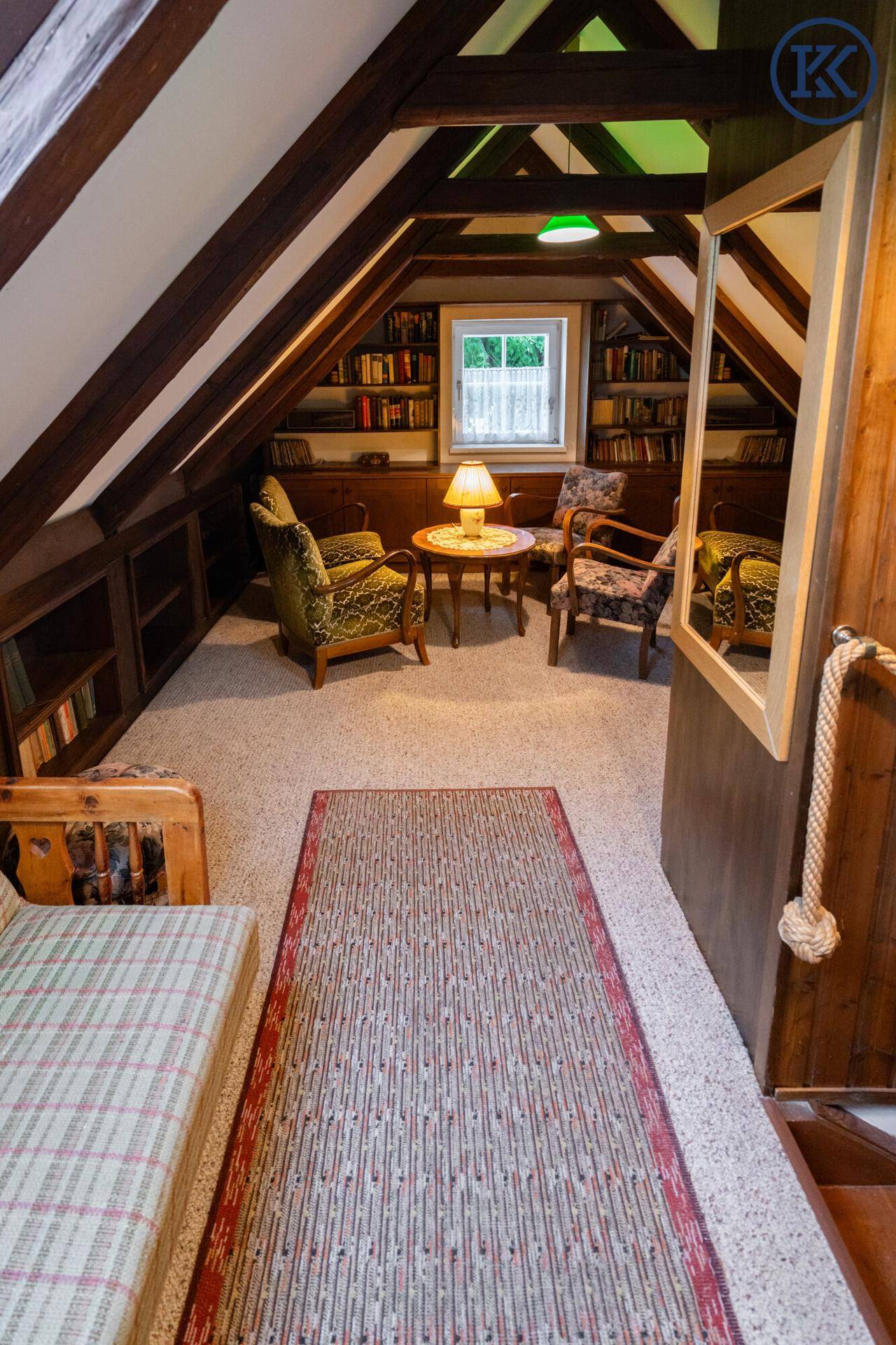 Gemütlicher Dachgeschossbereich mit Bücherregalen, Sesseln und Teppichboden, ideal als Leseecke.