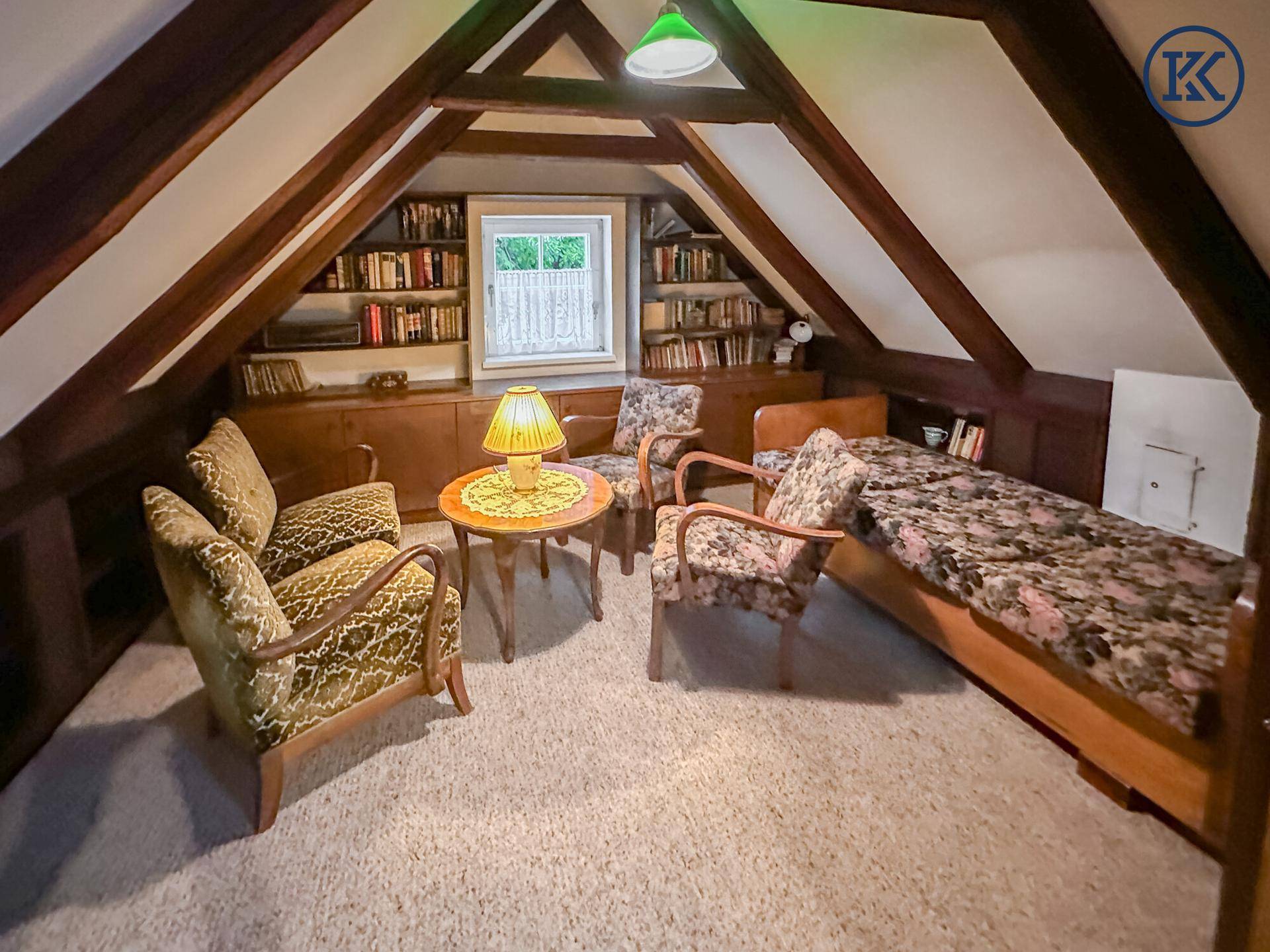 Gemütliches Dachzimmer mit sichtbaren Holzbalken, Teppichboden und integrierten Bücherregalen.