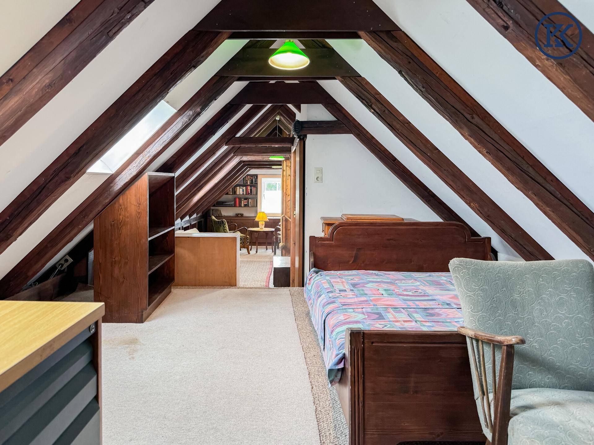 Offener Dachgeschossbereich mit Holzbalken, Bett und Blick in einen weiteren Wohnbereich.