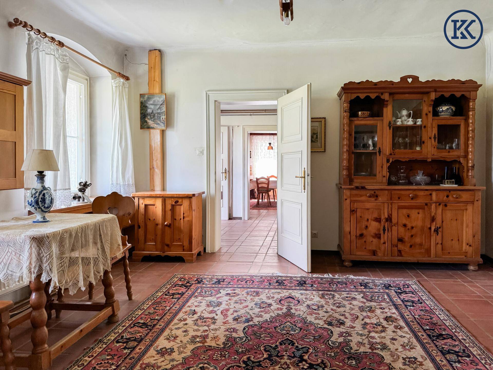 Traditionelles Wohnzimmer mit Terrakottafliesen, Holzmöbeln und Blick in den Essbereich.