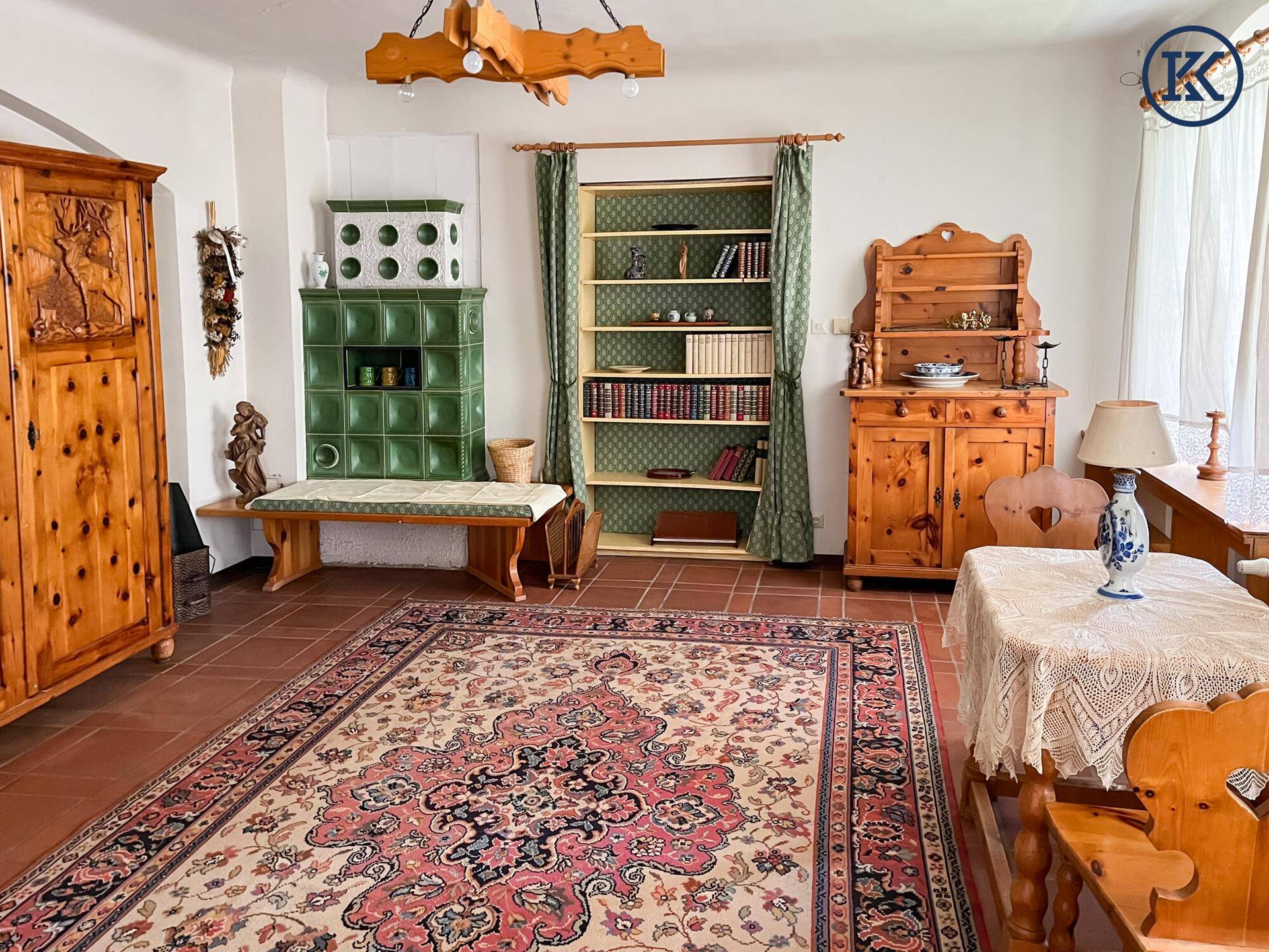 Geräumiges Zimmer mit Terrakottafliesen, grünem Kachelofen und traditionellen Holzmöbeln.