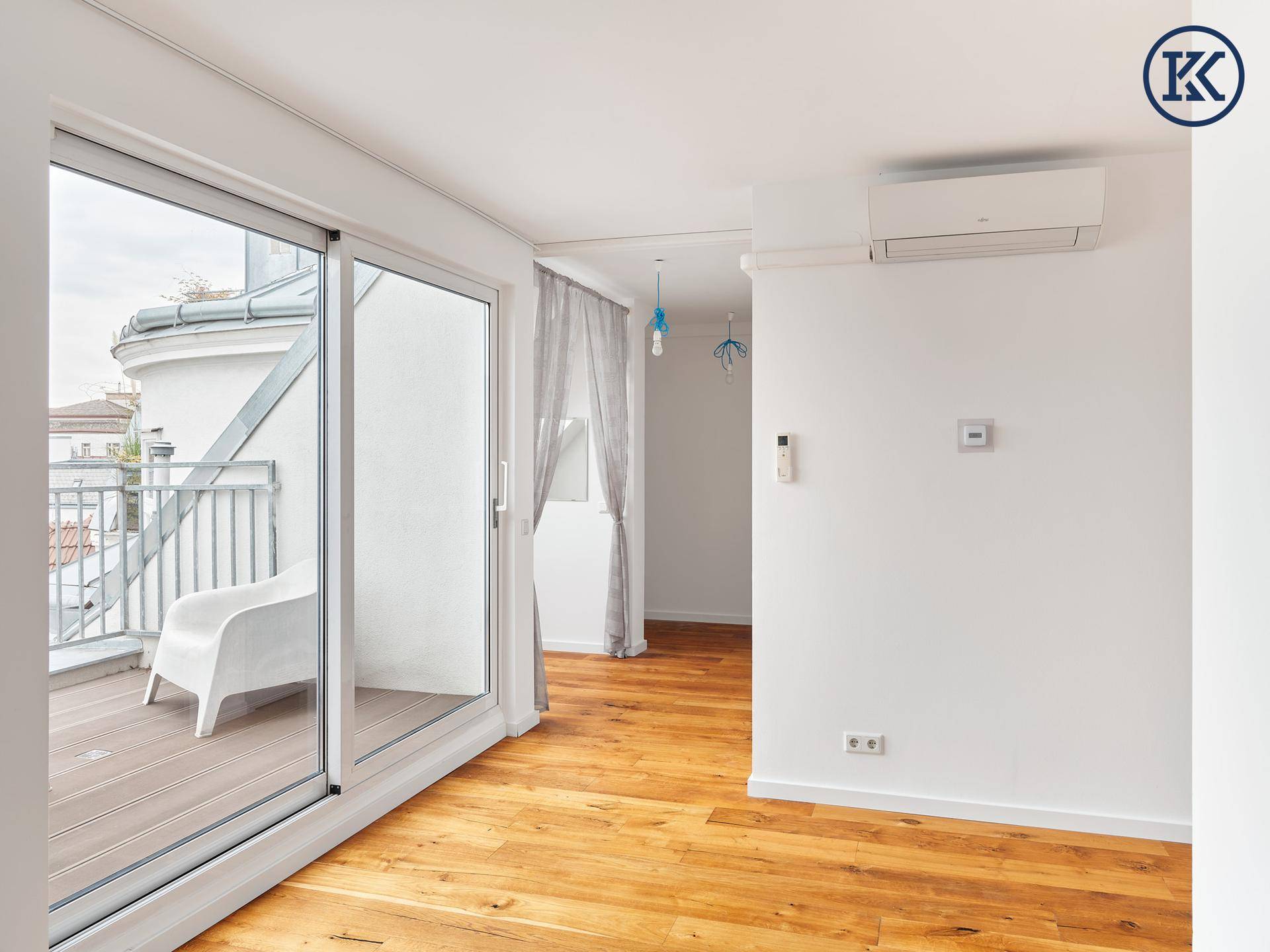Heller Raum mit Holzboden, Klimaanlage und Schiebetür zum Balkon.