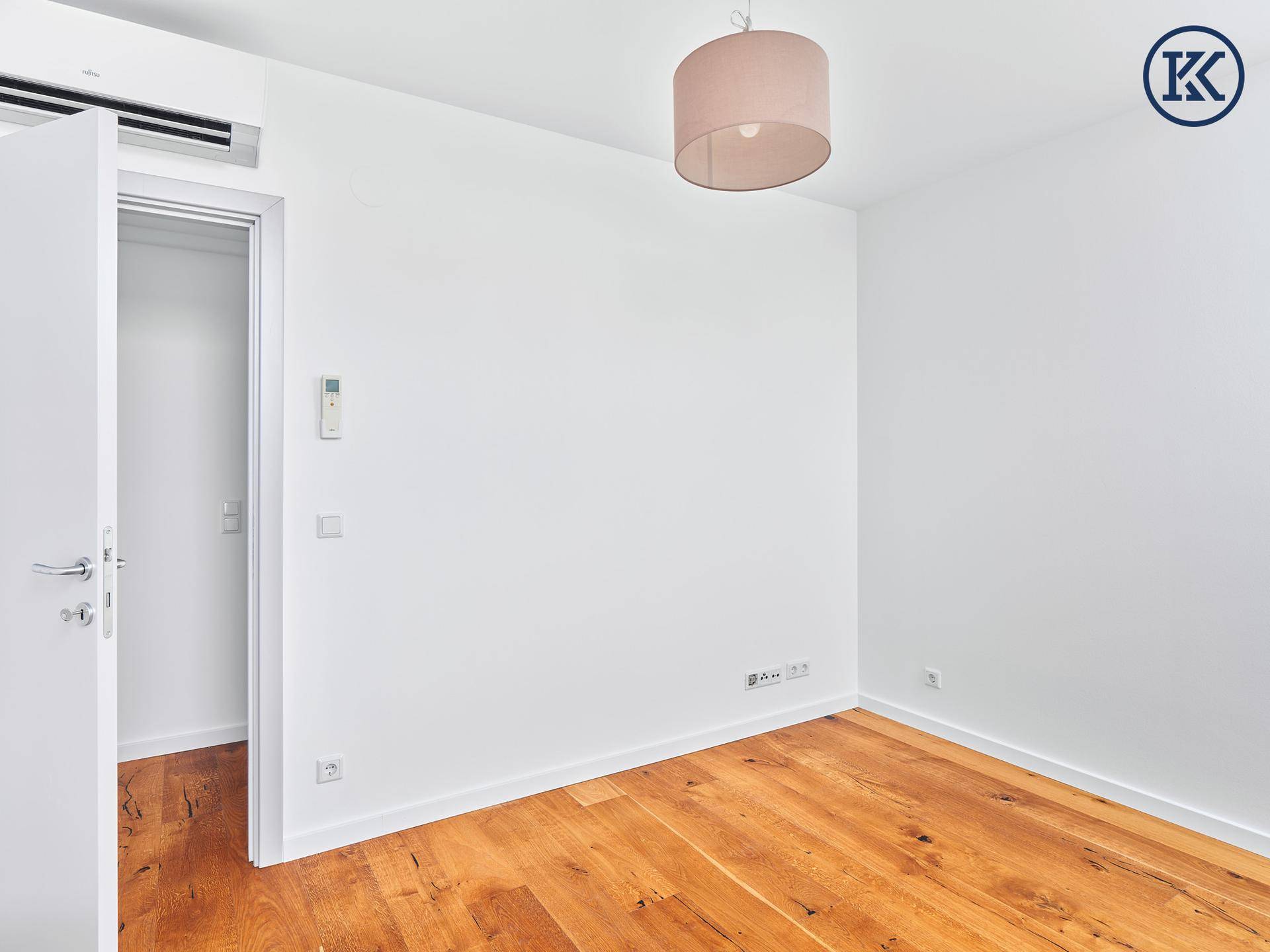 Helles Schlafzimmer mit Holzboden, Klimaanlage und Zugang zu einem Ankleidebereich.