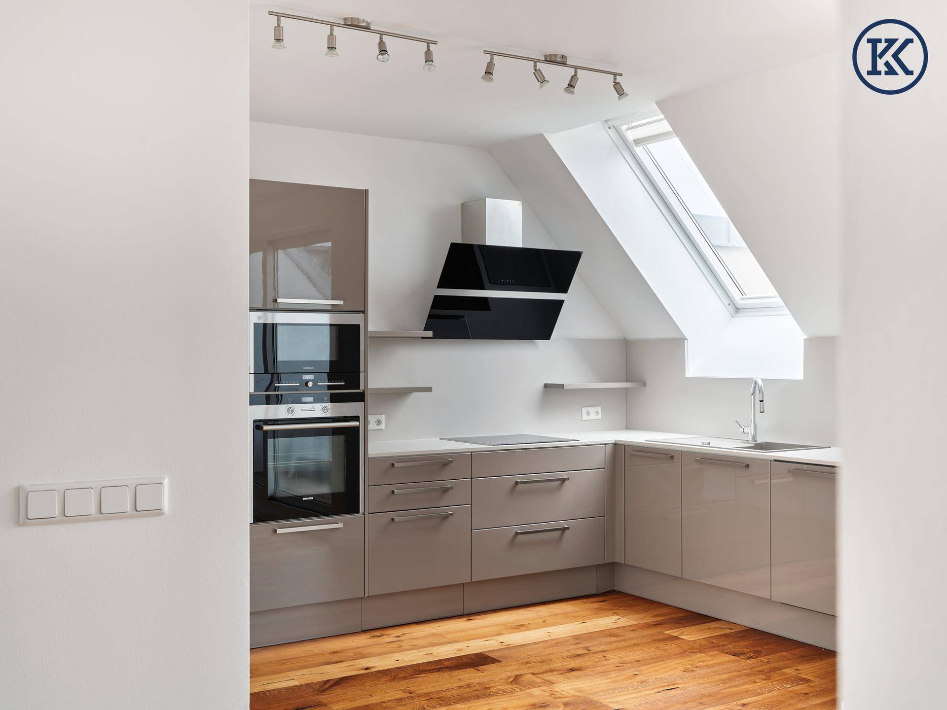 Moderne Küche mit Einbaugeräten, Dachfenster und glänzenden Schränken.